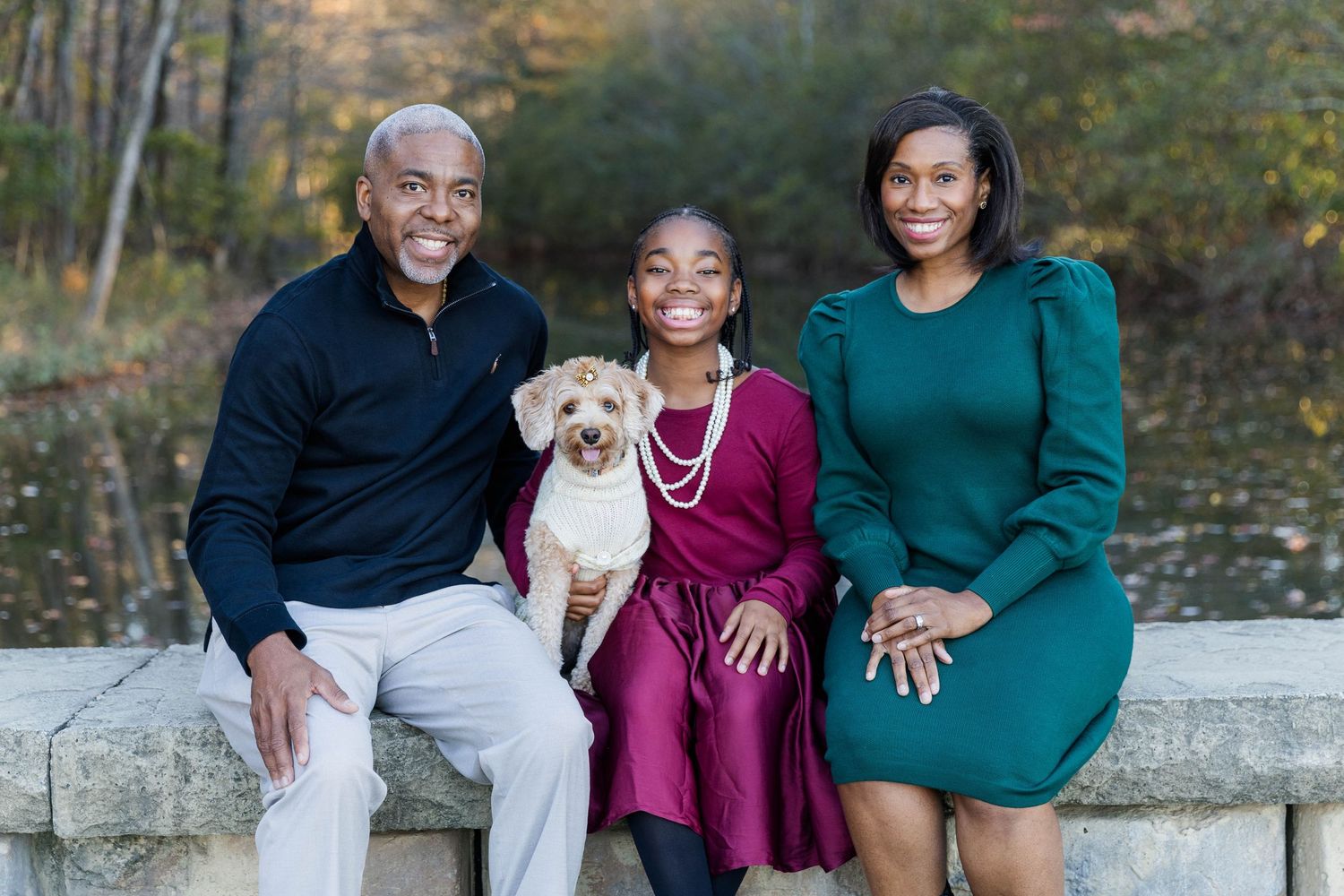 Family poses together outdoors with small dog during autumn photoshoot.