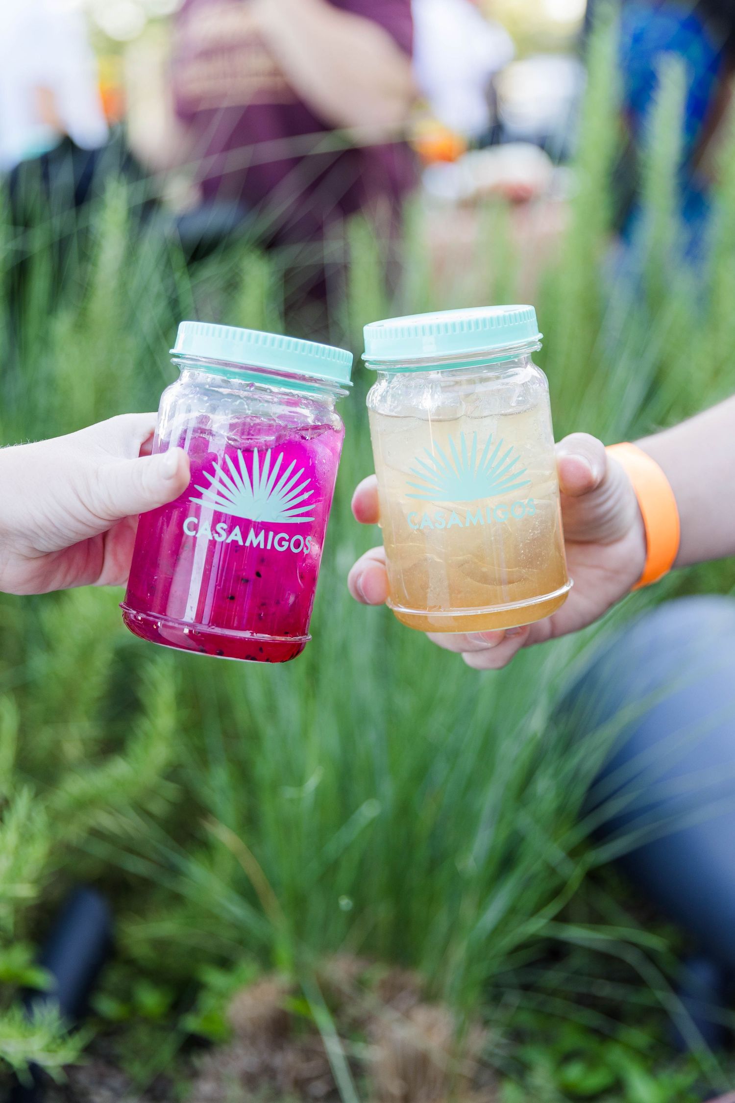 Colorful cocktails in mason jars being held up for a celebratory toast outdoors.