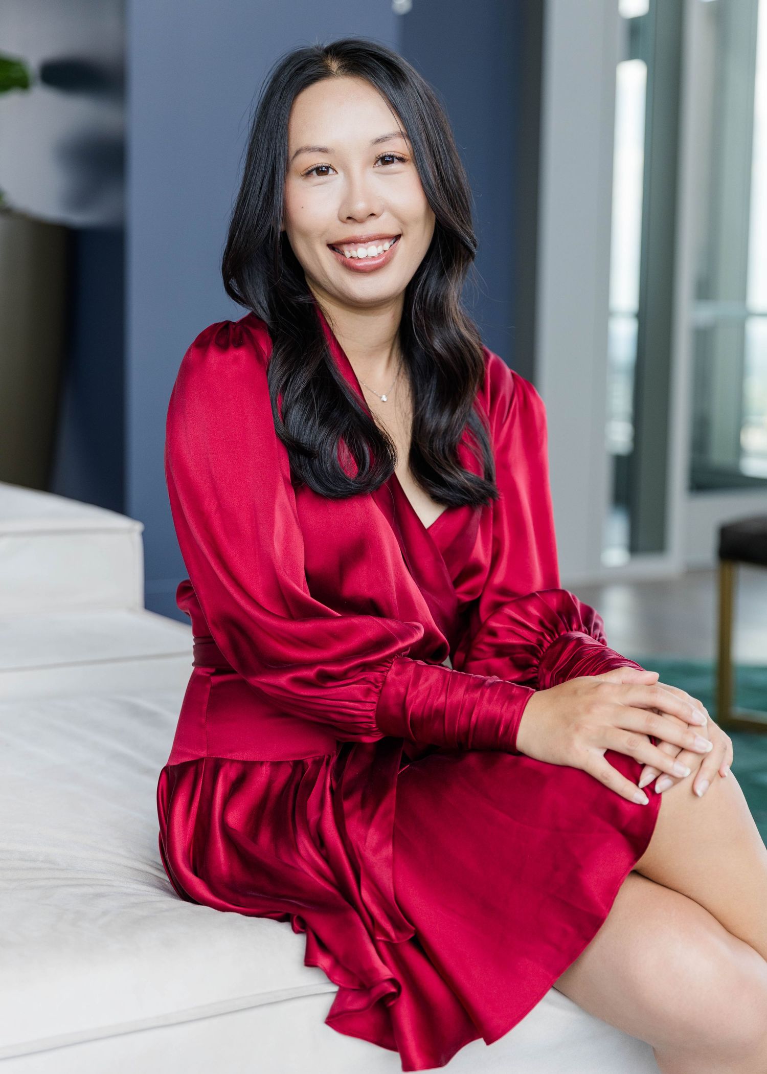 Woman in red silk robe poses elegantly on white furniture in modern interior setting.
