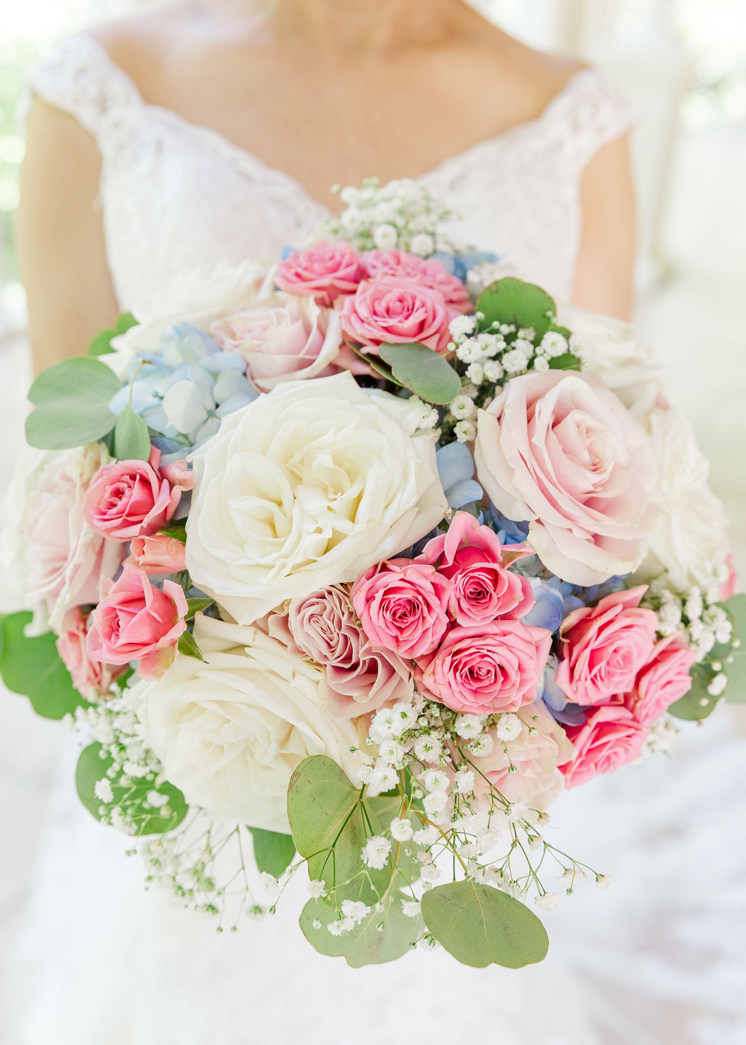 Bride holding a lush wedding bouquet with pink and white roses, baby's breath, blue hydrangeas, and eucalyptus leaves.