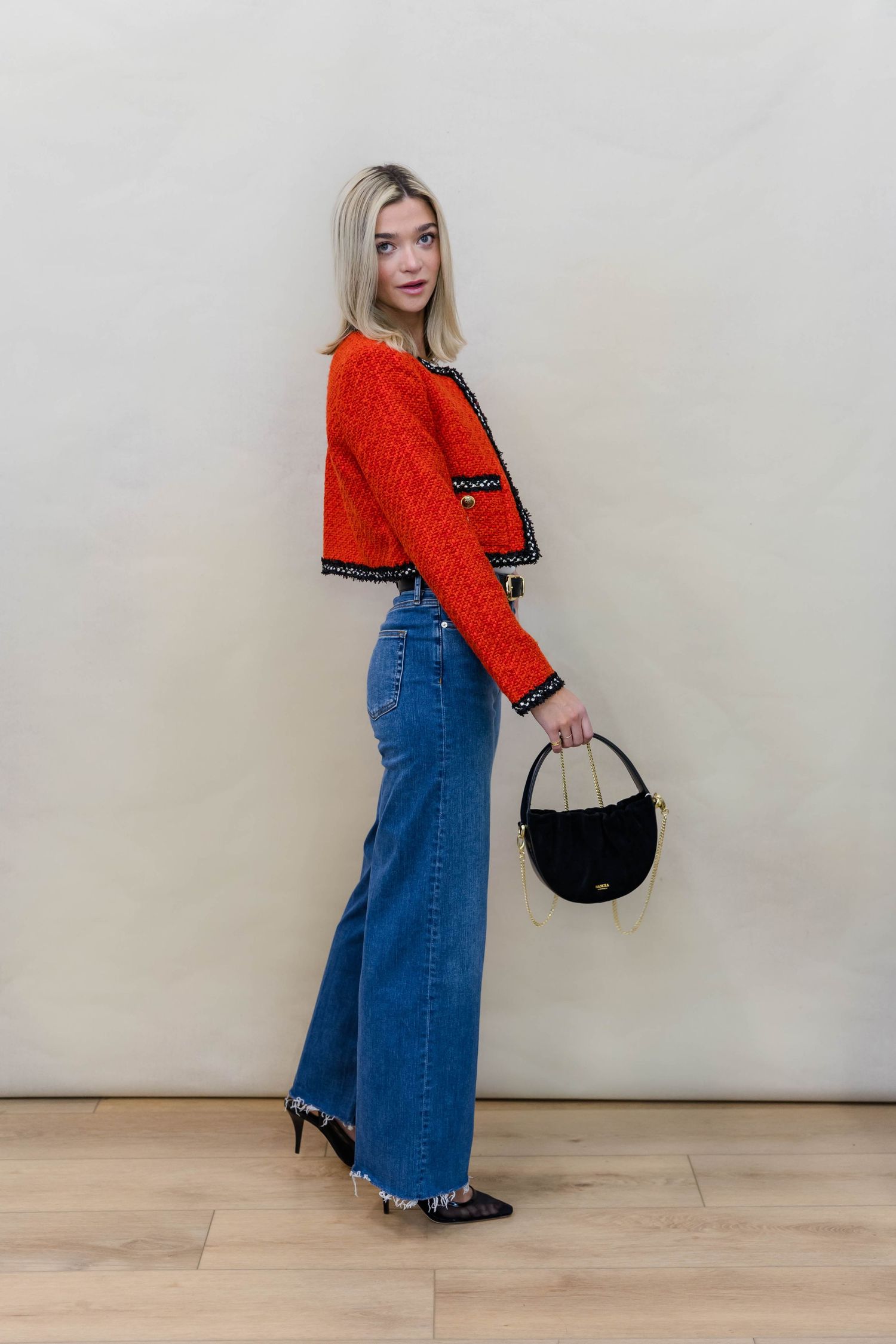 Red knit sweater and flared jeans accessorized with black handbag in retro-inspired outfit.