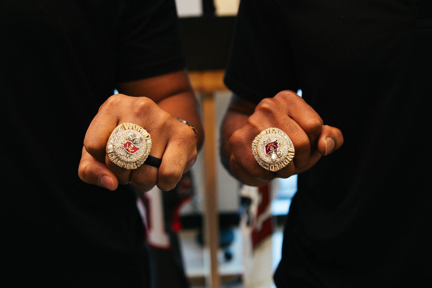 Close-up shot of hands displaying championship rings against a dark background.
