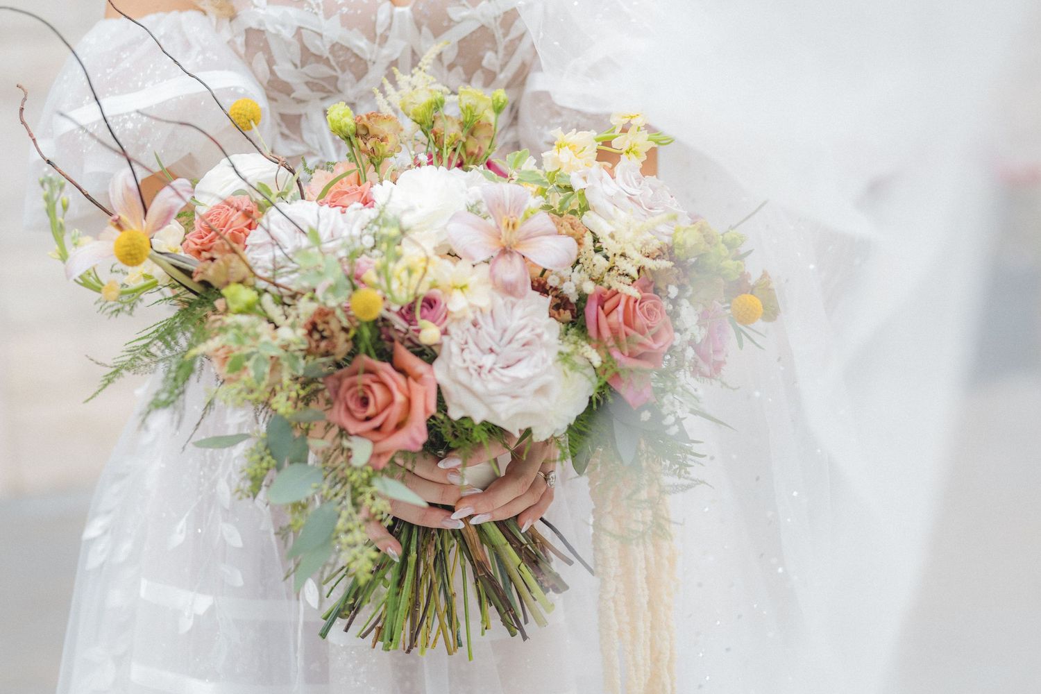 Elegant wedding bouquet featuring pink roses, white dahlias, and delicate greenery with trailing silk ribbons.