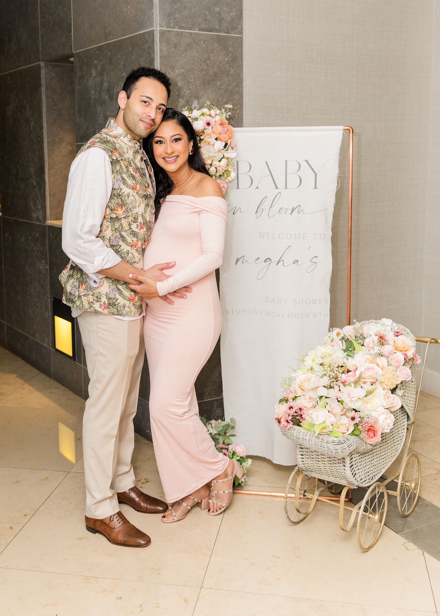 A pink and white themed baby shower setup with floral decorations and a decorative carriage.