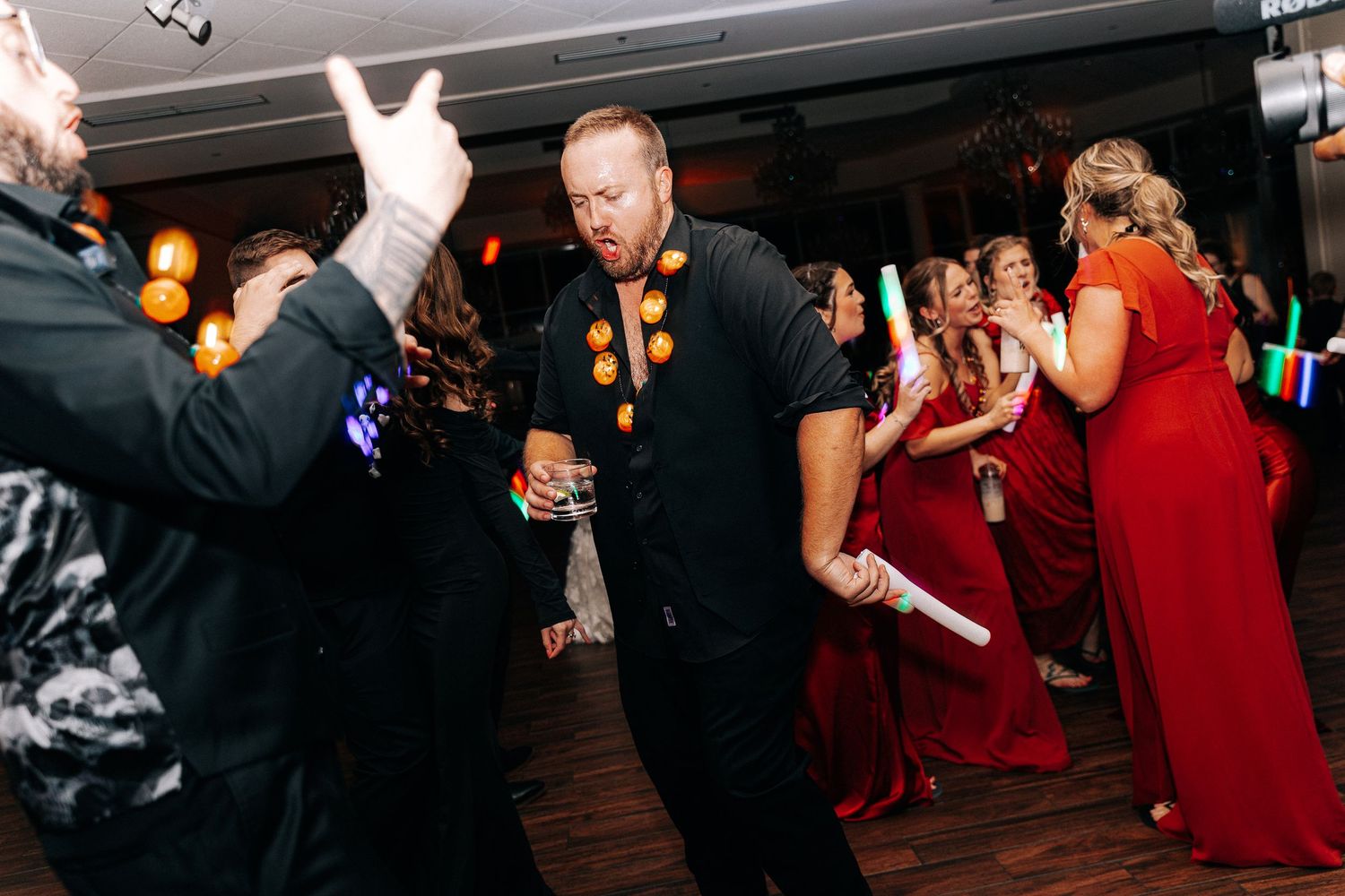 Guests dancing energetically at a wedding reception, wearing formal attire including red gowns and black suits.