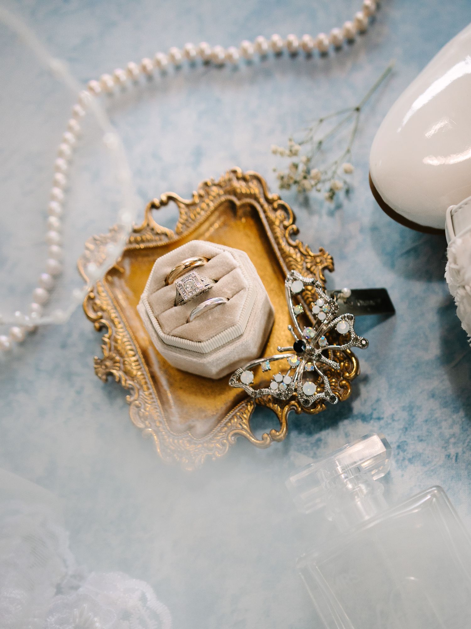 Vintage-style wedding details with pearl strands and gold frames on light blue surface.