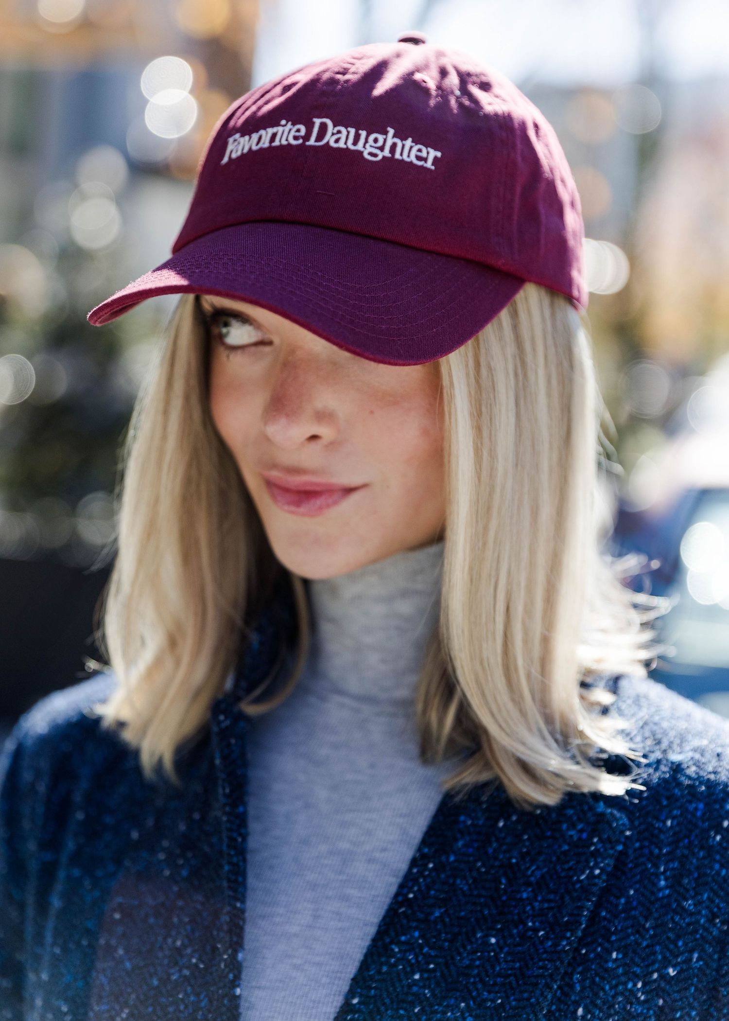 Burgundy baseball cap with text worn with gray turtleneck and navy coat.
