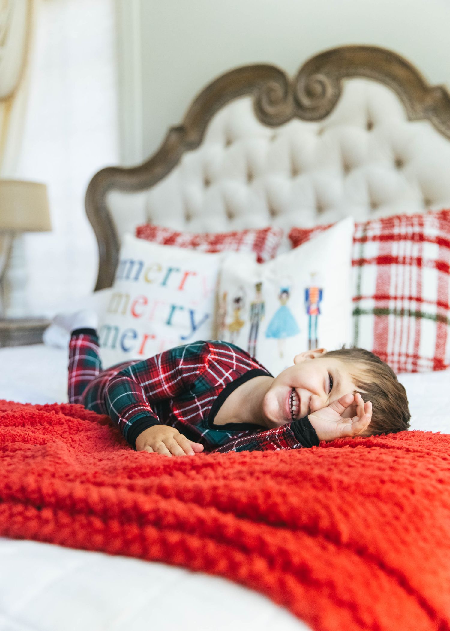 Holiday photo session with red plaid pajamas and cozy blanket on white bed.