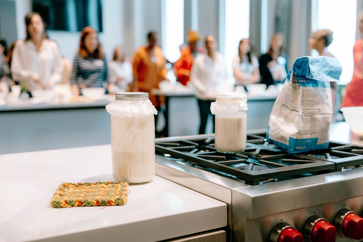 A modern cooking demonstration event with multiple workstations and people gathered in a bright kitchen space.