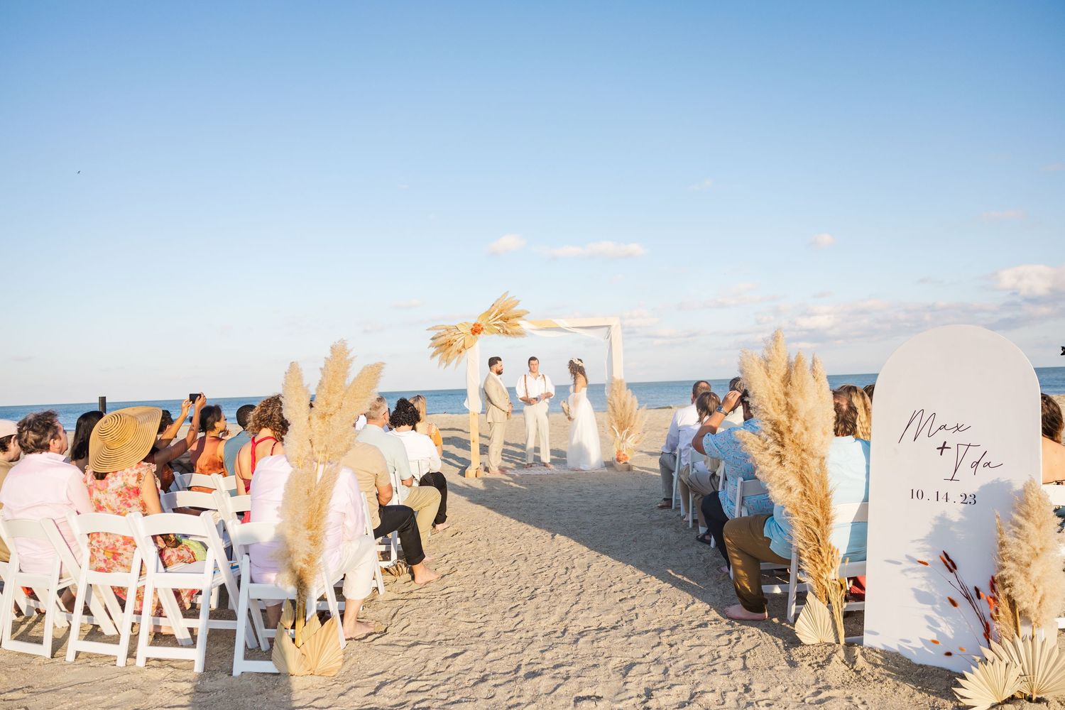 A beach wedding ceremony setup with white chairs and decor against a bright blue sky.