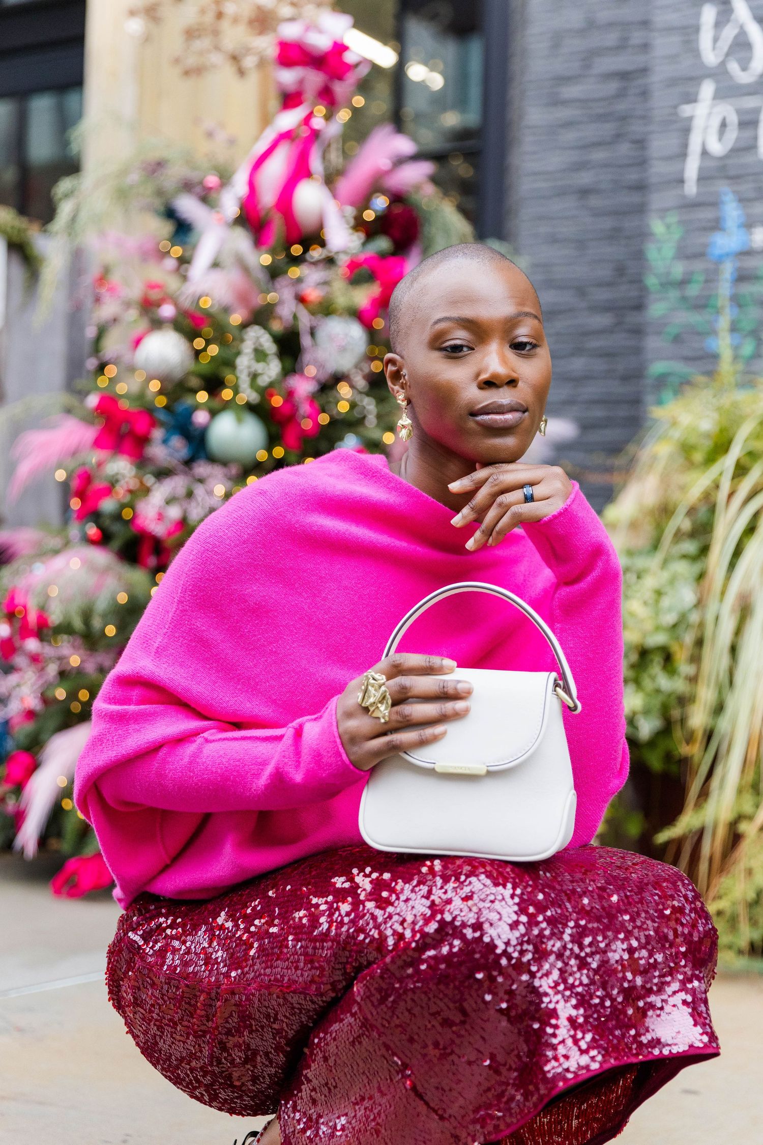 Hot pink sweater paired with sparkly burgundy skirt and white handbag against urban backdrop.