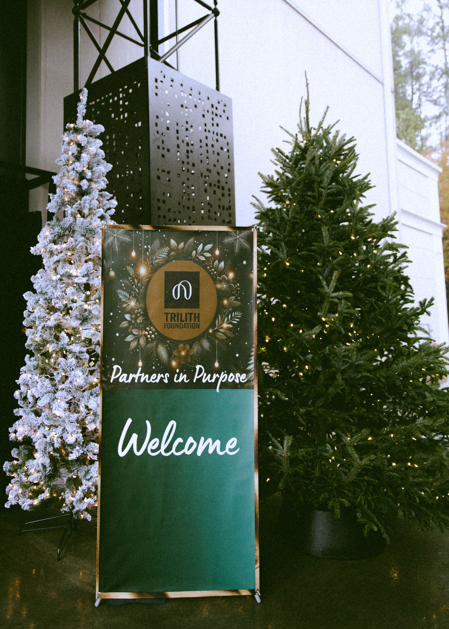 Welcome sign display with evergreen trees and white floral decorations.