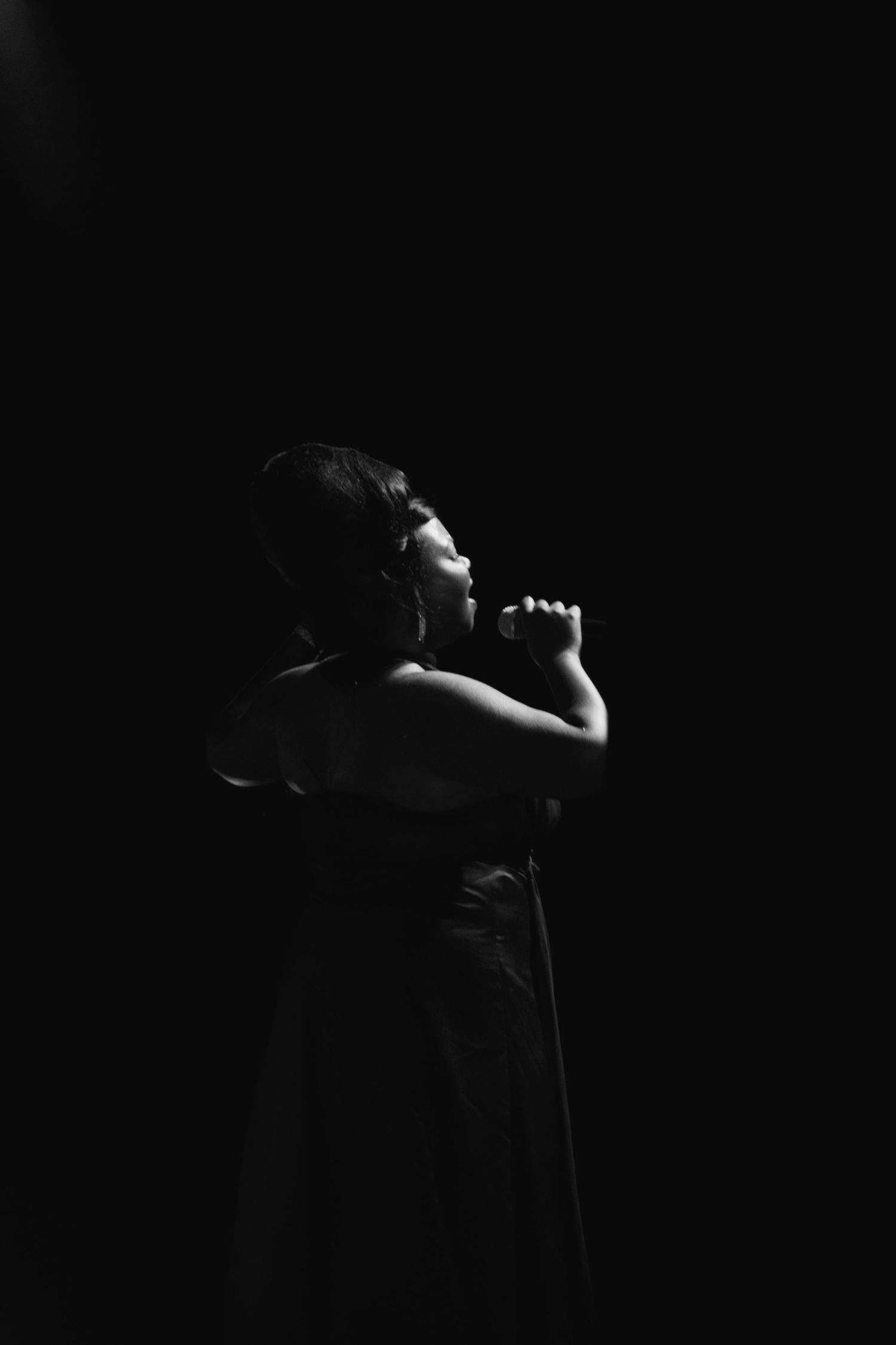 Dramatic low-key portrait of a performer in silhouette against dark background.