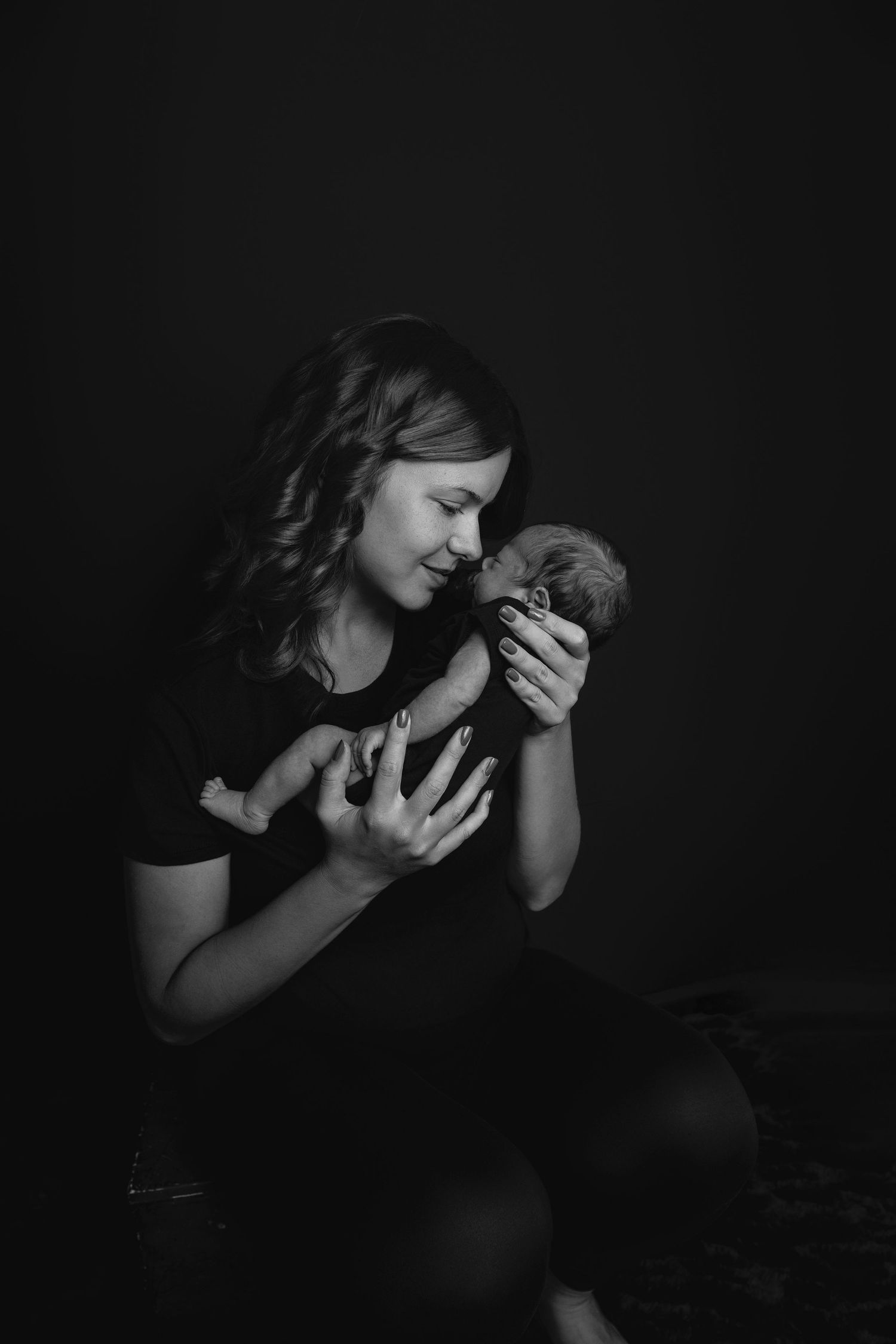 Dramatic low-key portraits capturing intimate moments with newborn in black and white.