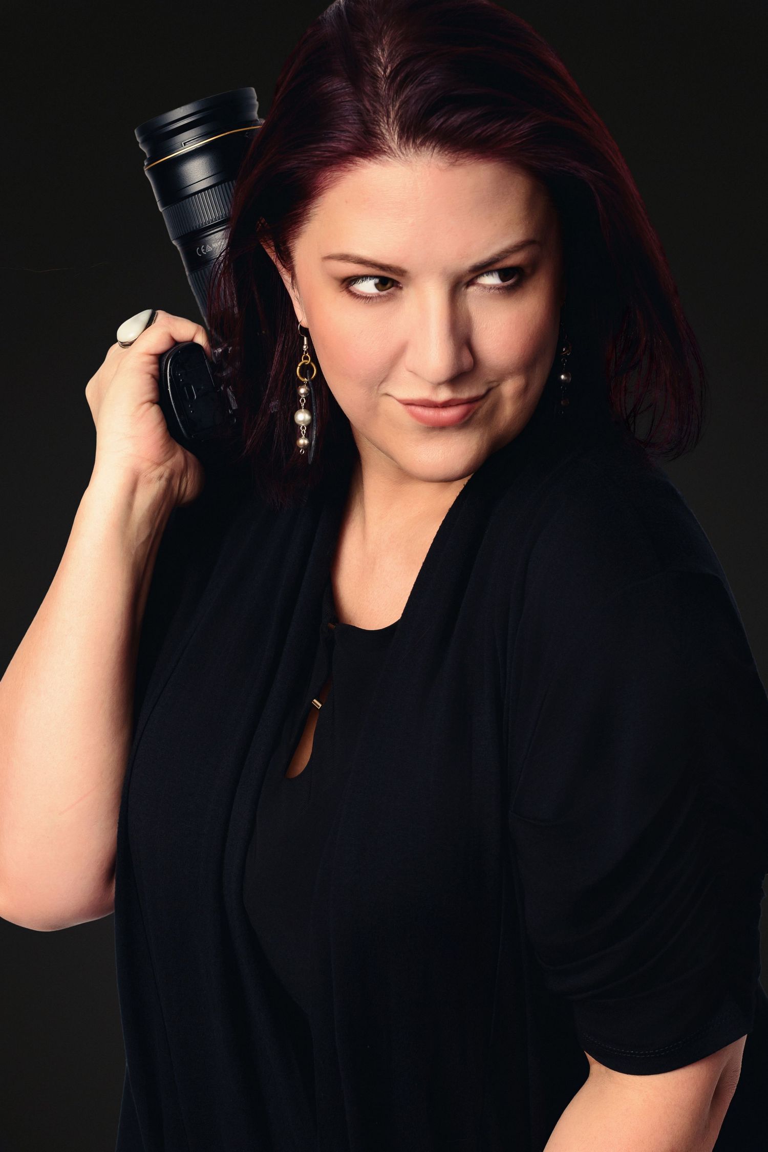 Portrait series featuring photographer holding camera lens against dark background.
