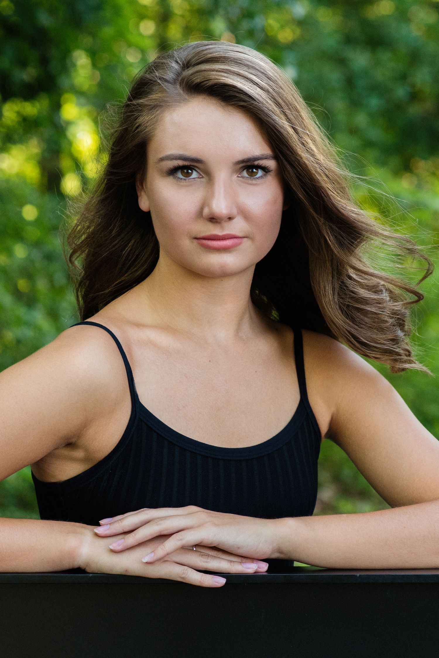 Glamour portraits with flowing hair and black top against natural bokeh background.