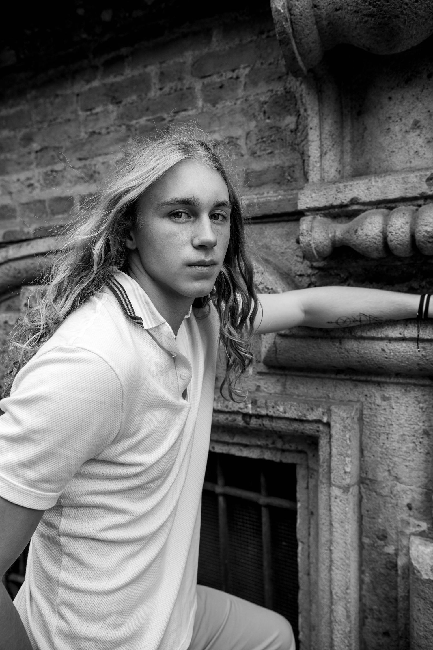 Black and white portrait against brick wall featuring casual polo shirt styling.