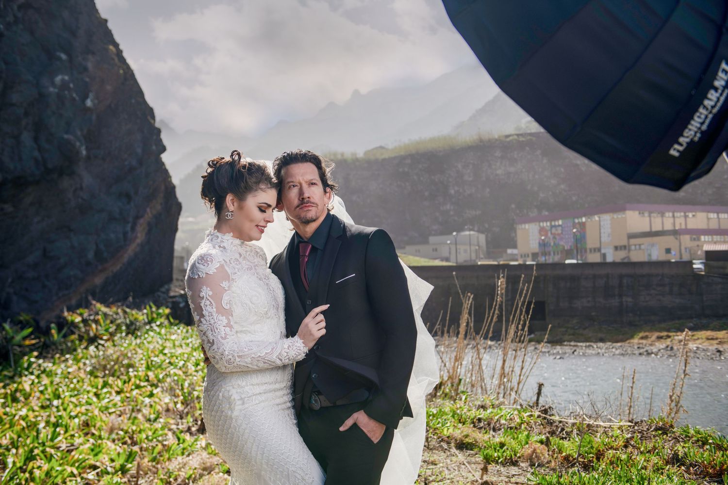 Wedding couple embraces tenderly against cloudy mountain backdrop.
