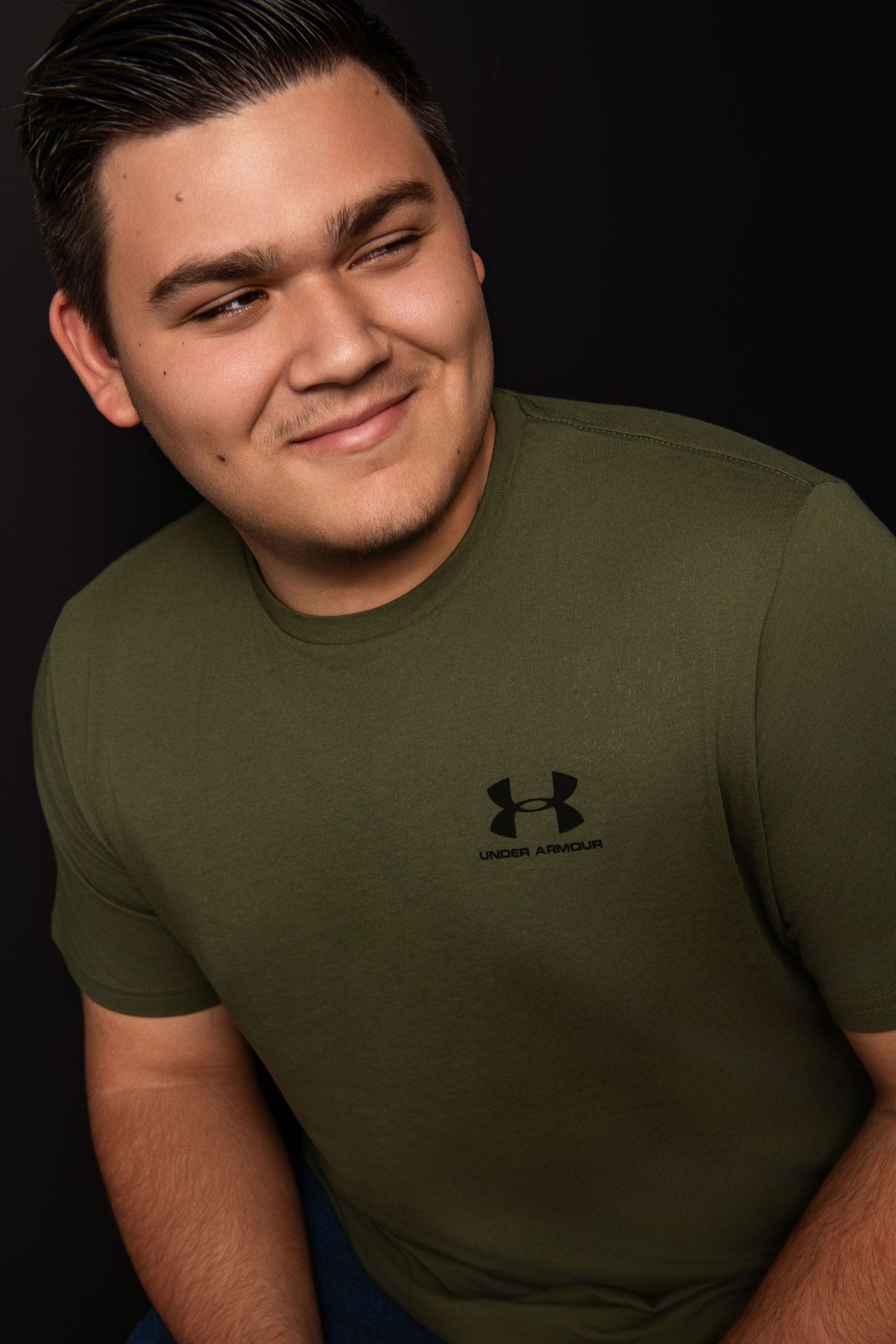 Casual headshot of a person wearing an olive green Under Armour t-shirt against a dark background.