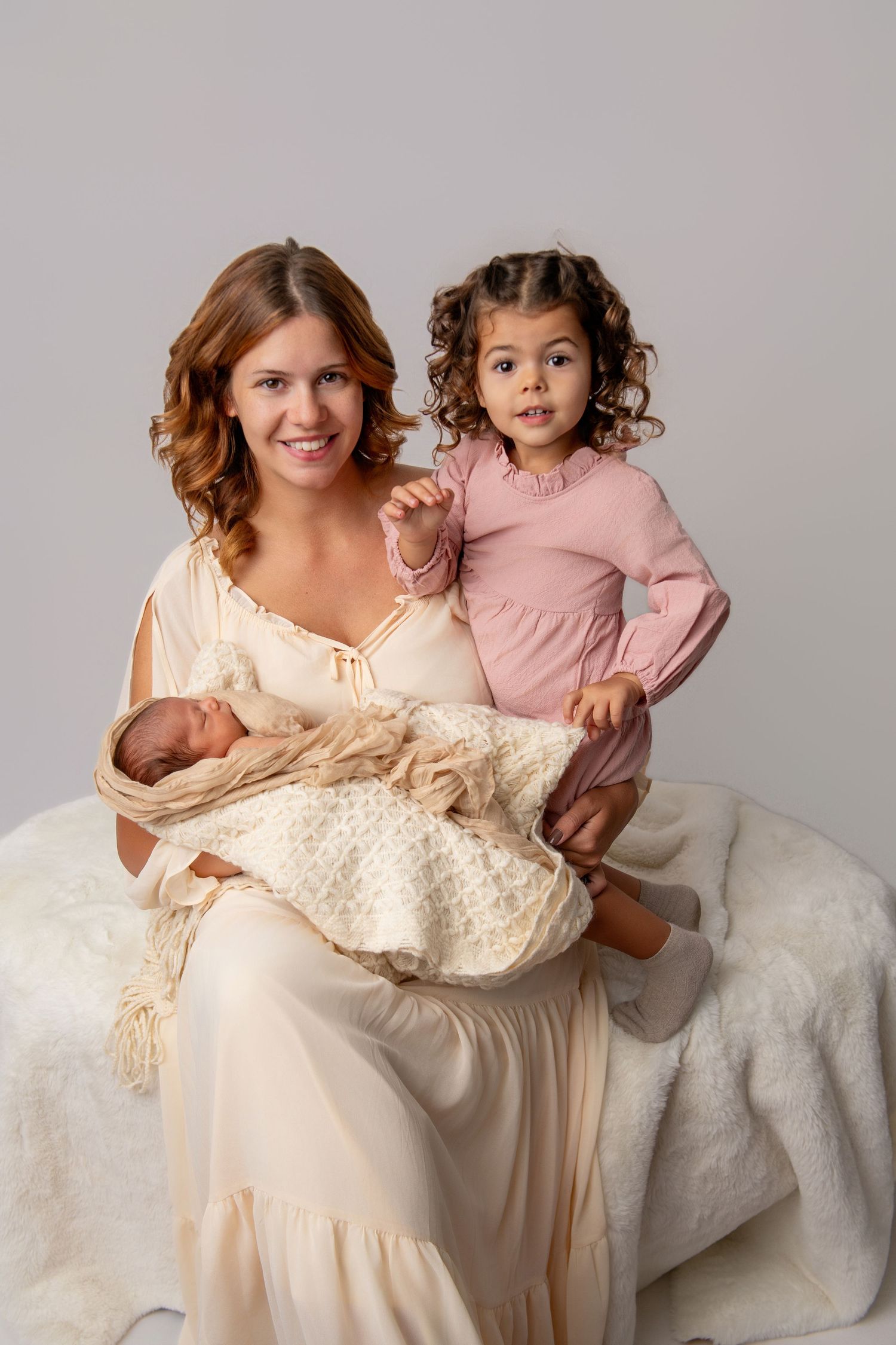Mother and children posed in cream and pink dresses for elegant studio portraits.