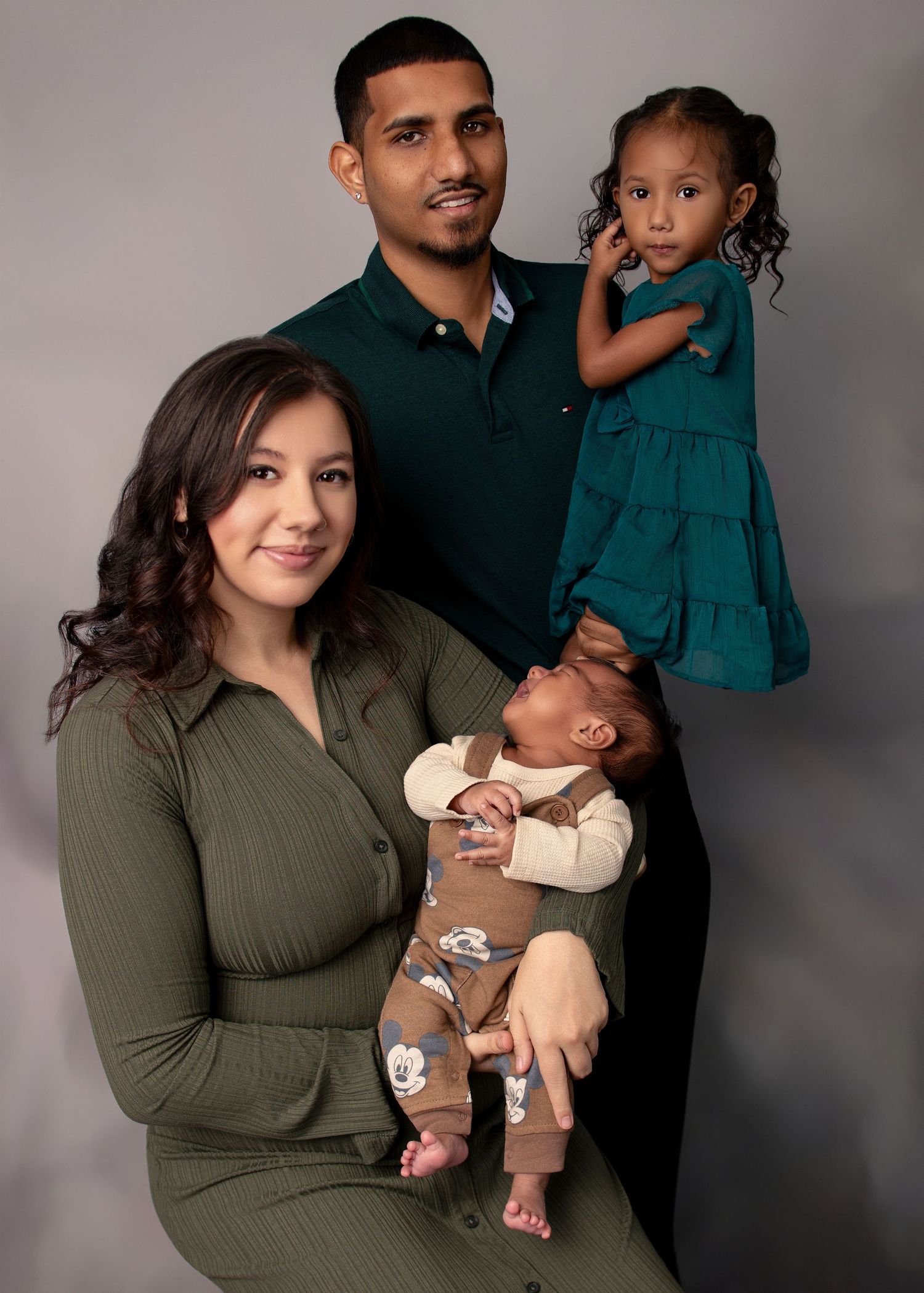 Studio family portrait session with coordinated outfits in green and black against grey background.
