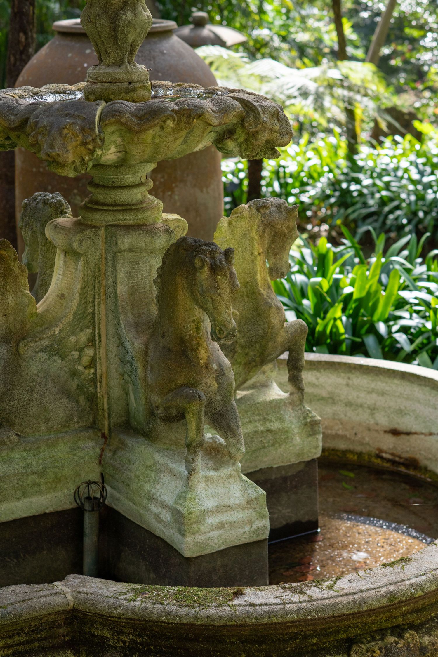 Ancient stone fountain with moss and weathered details in a garden setting.