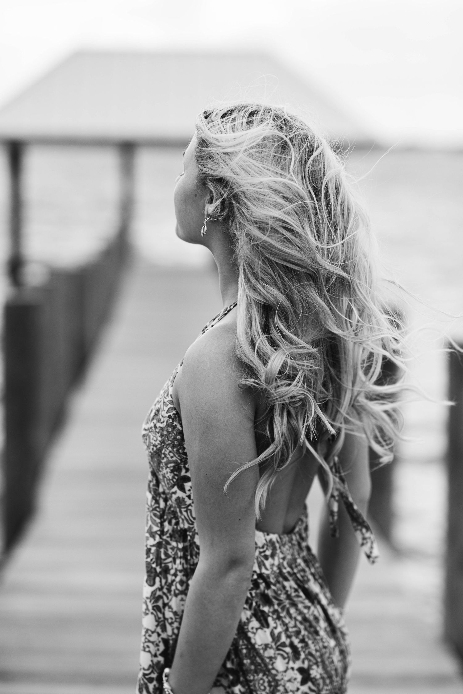 Black and white portrait of flowing blonde hair against seaside dock backdrop.