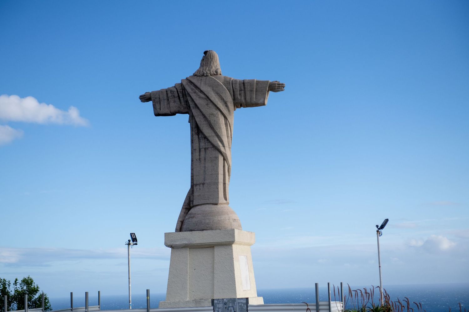 Large Christ statue monument silhouetted against bright blue sky overlooking ocean vista.