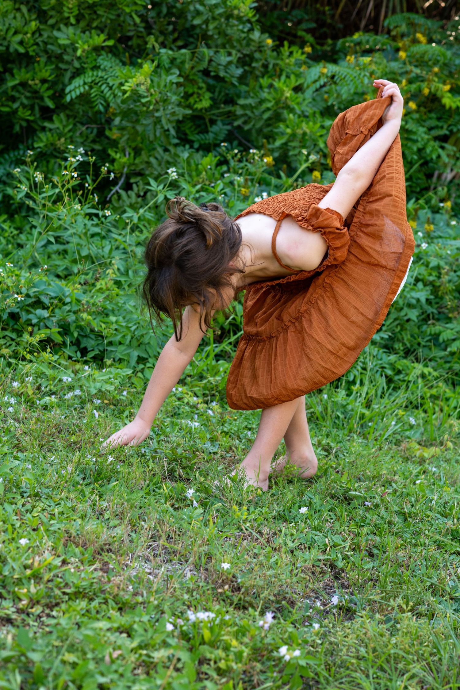 Sequence showing playful child in brown dress twirling and dancing in green garden.