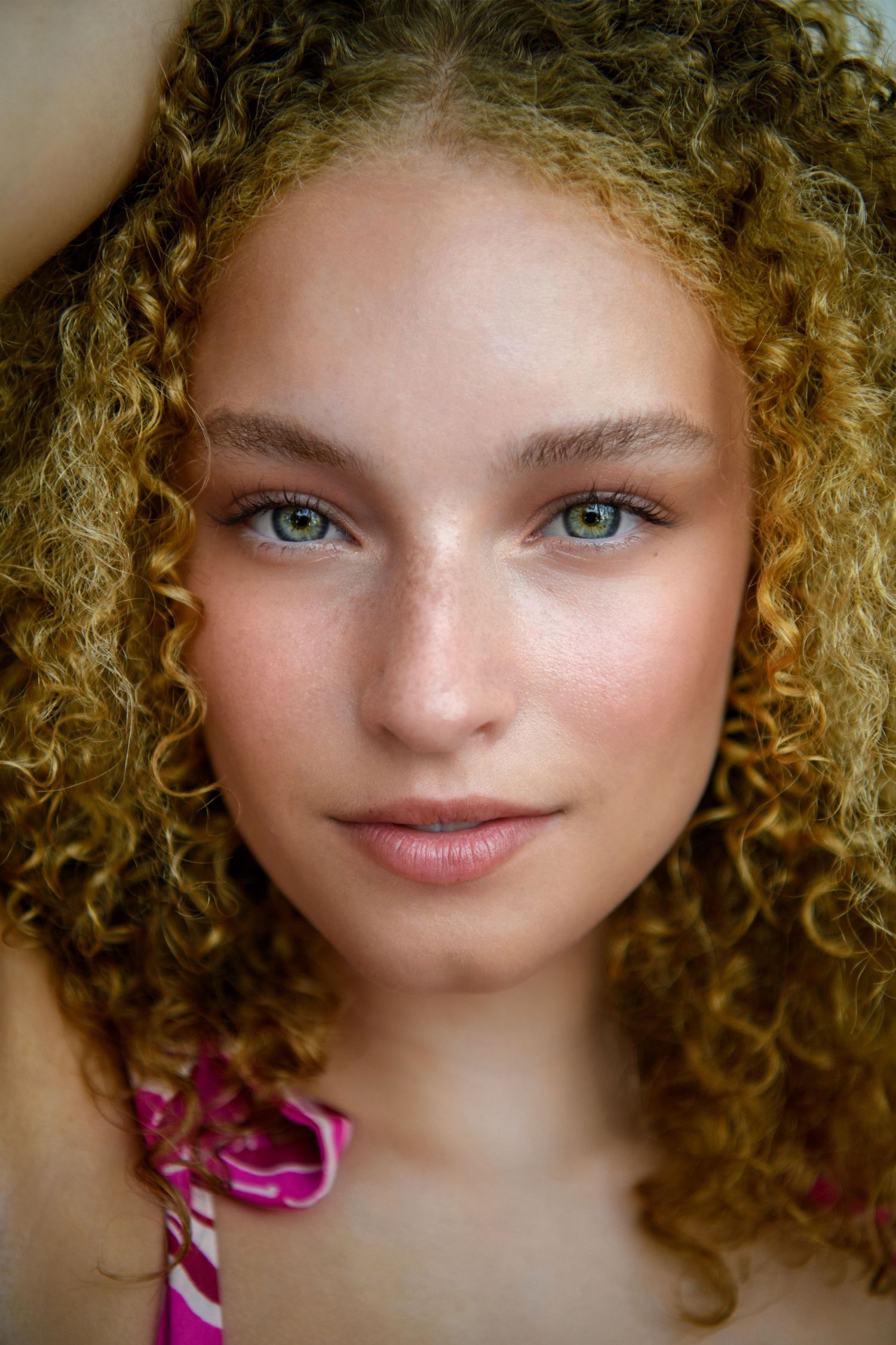Close up beauty portrait featuring curly blonde hair and natural makeup.