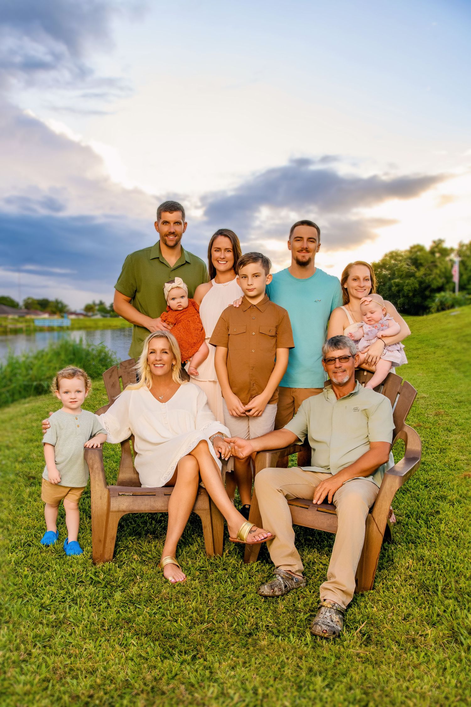 Extended family sitting together on grassy hill during golden hour sunset photoshoot.