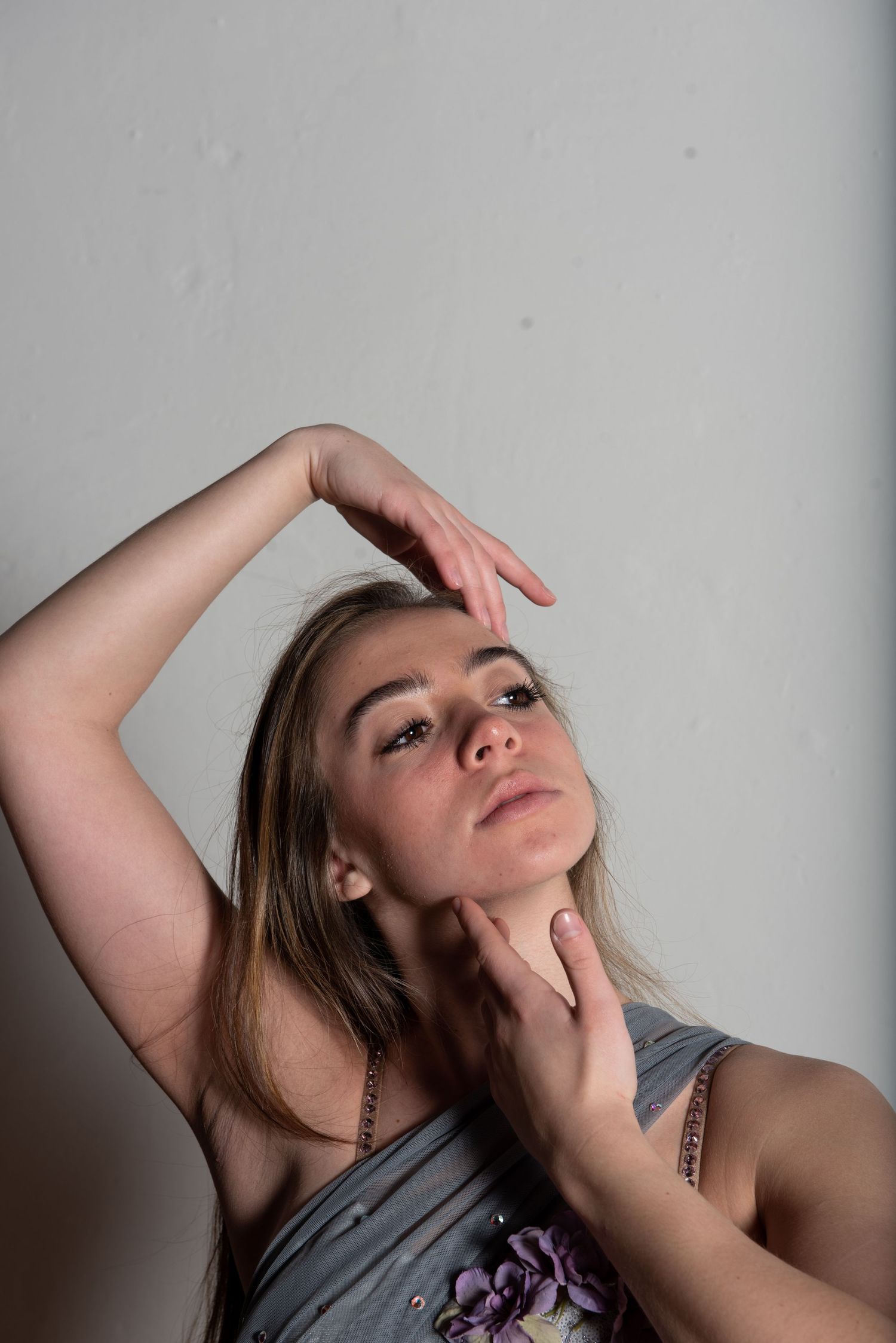 Portrait of a person in artistic pose against grey wall wearing grey top.