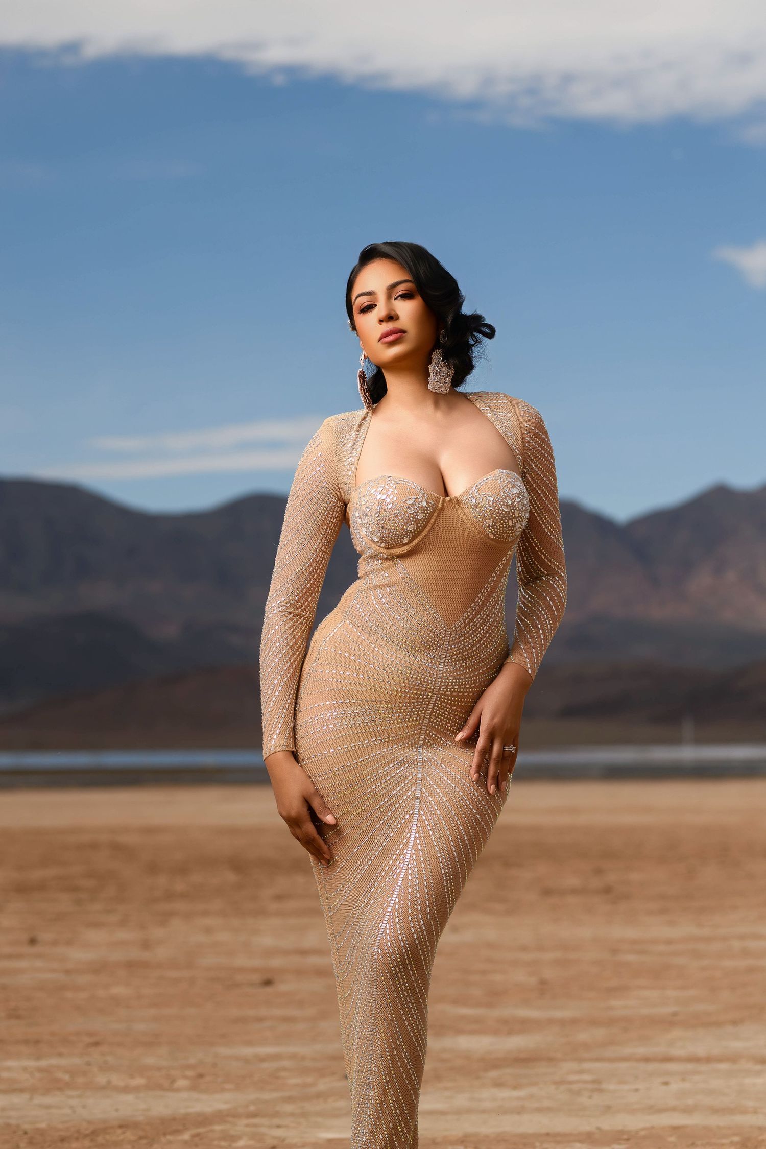 Desert fashion photography with beige fitted dress against mountain landscape.