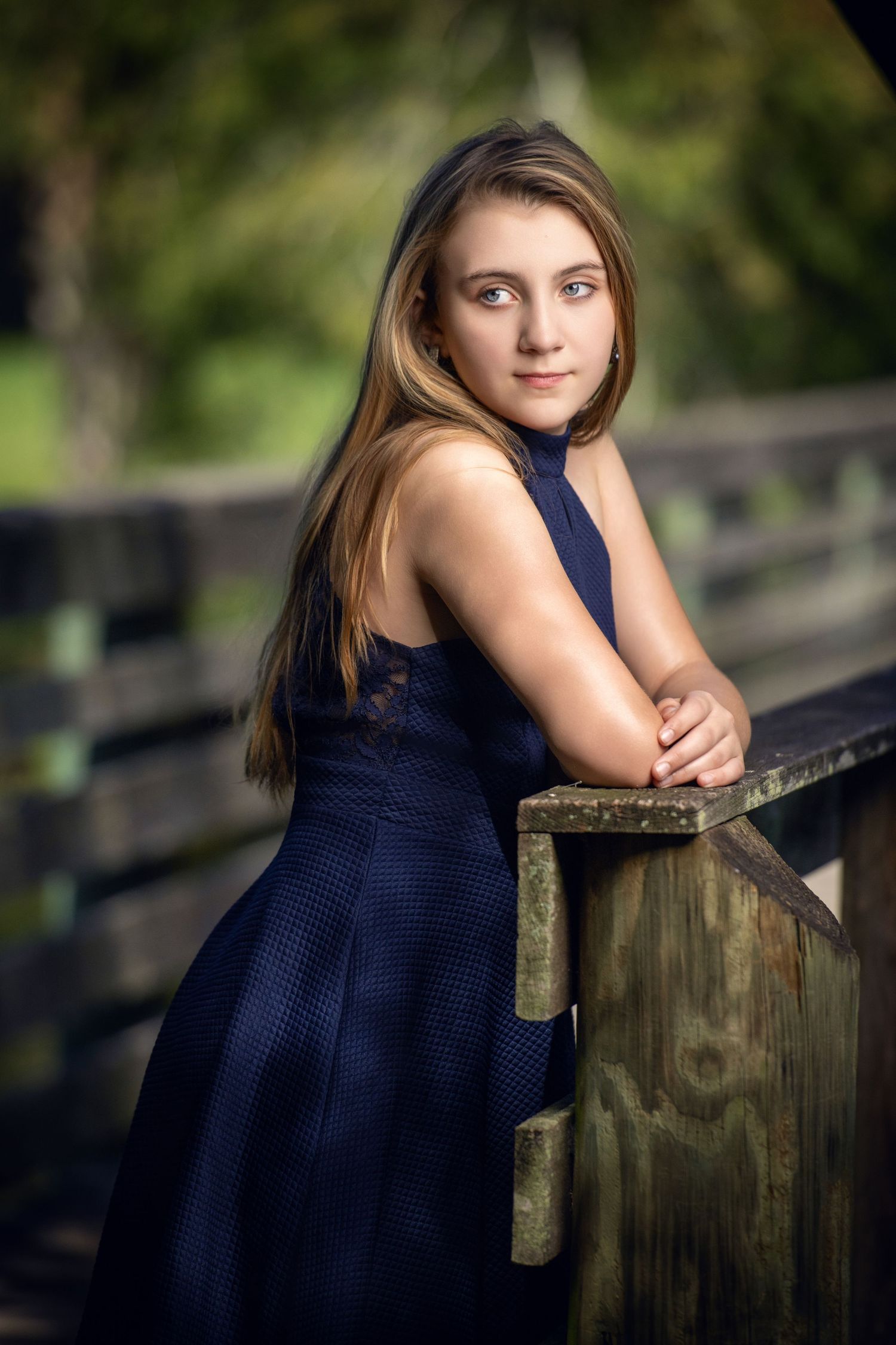 A person in a navy dress poses against a wooden fence in an outdoor setting.