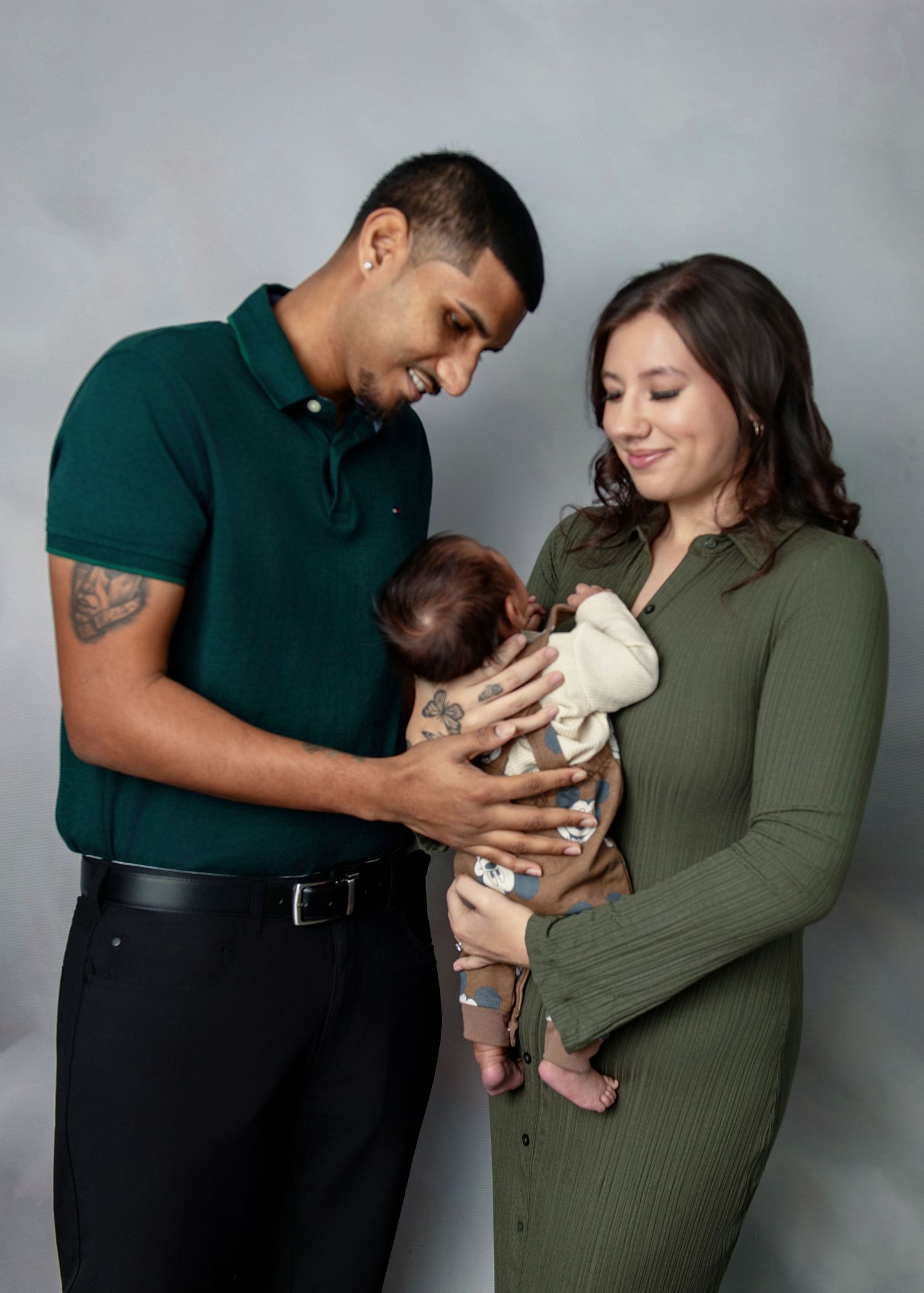 A series of tender moments showing a couple holding and bonding with their newborn baby against a gray backdrop.