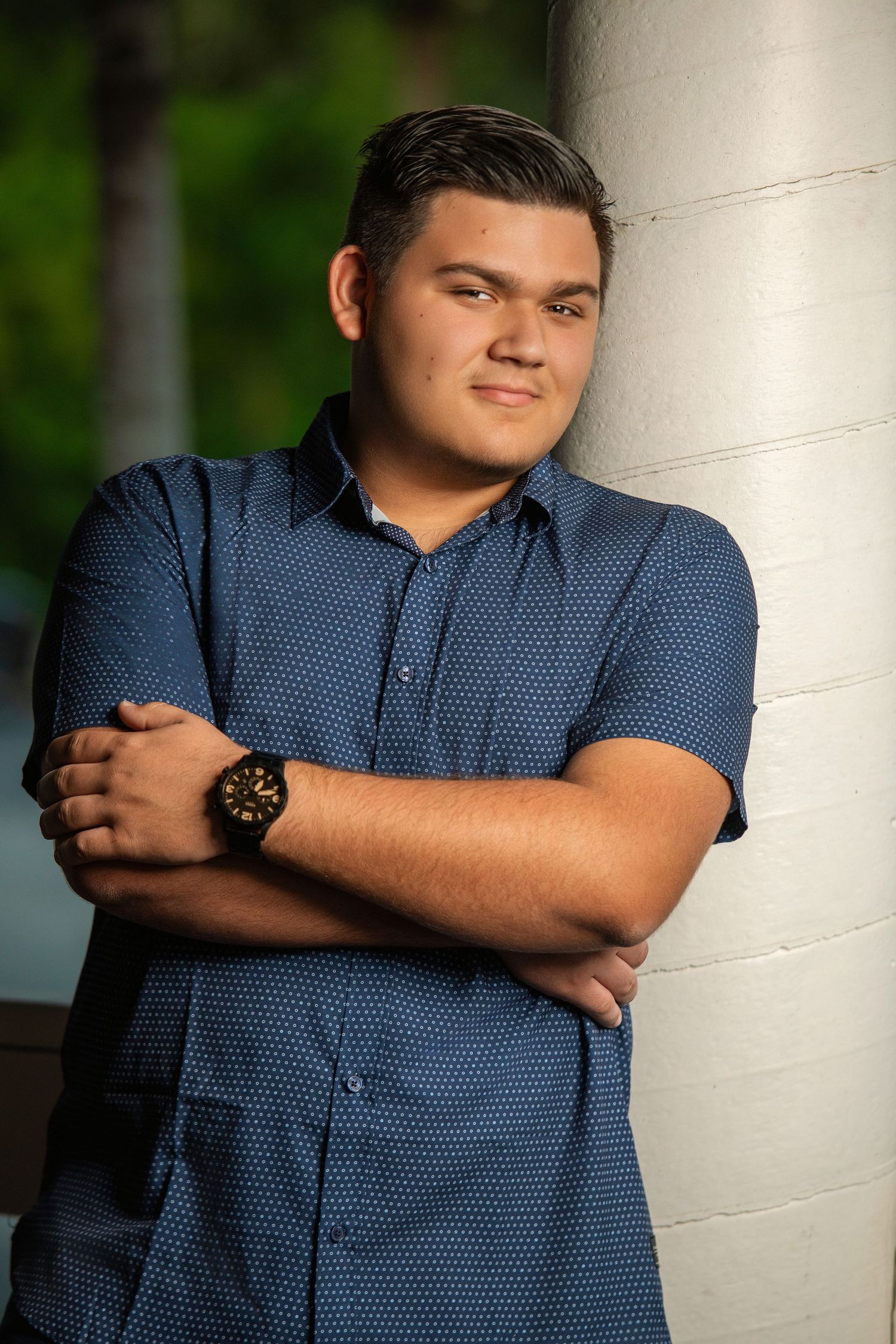Outdoor portrait of a person in a blue patterned shirt leaning against a white column.