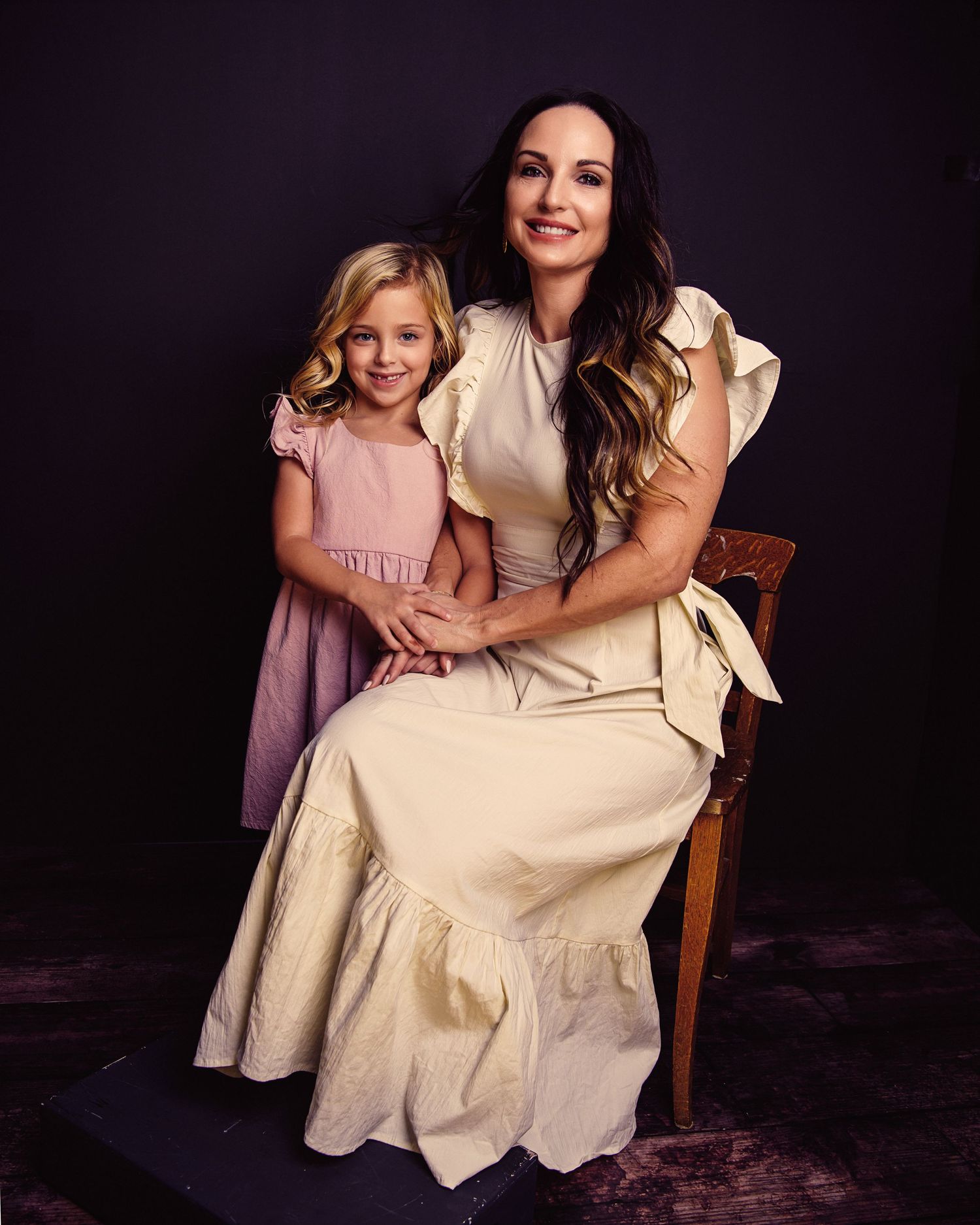 Heartwarming family portrait in matching cream-colored dresses against dark backdrop.