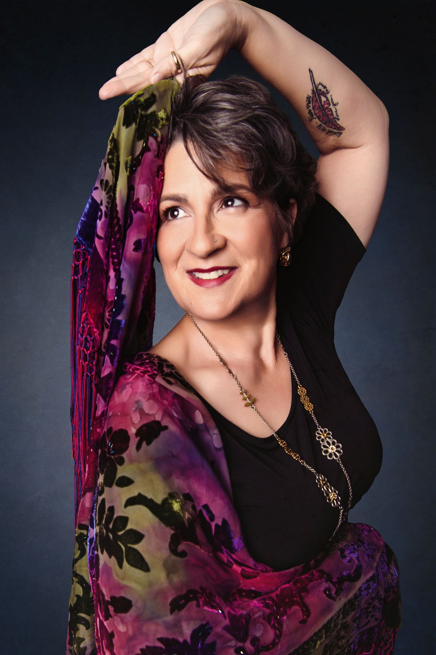 Fashion portrait series with model wearing black top and vibrant floral print against dark backdrop. Celebrating belly dance and aging