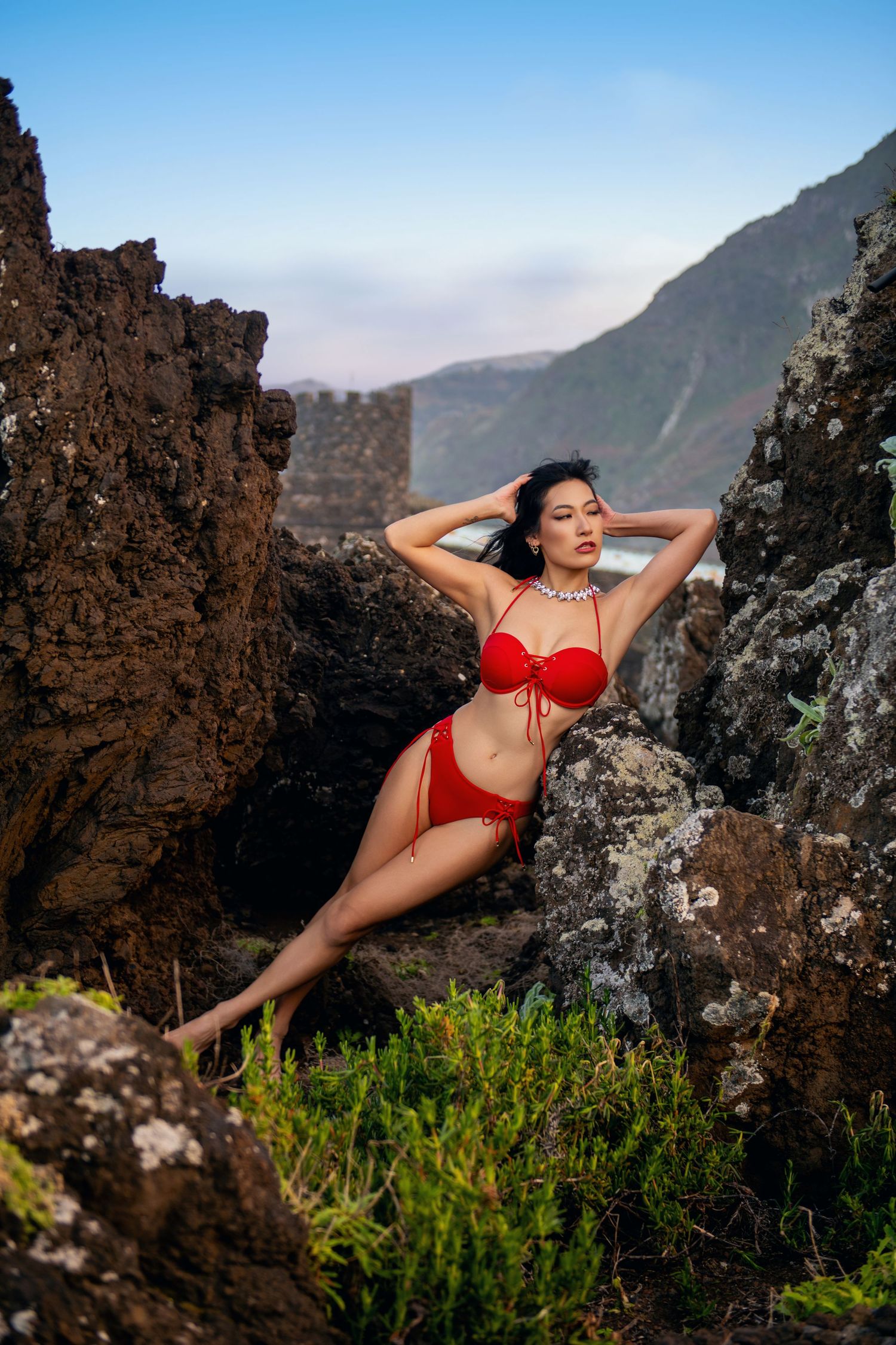 Woman in red swimwear poses elegantly among coastal rock formations.