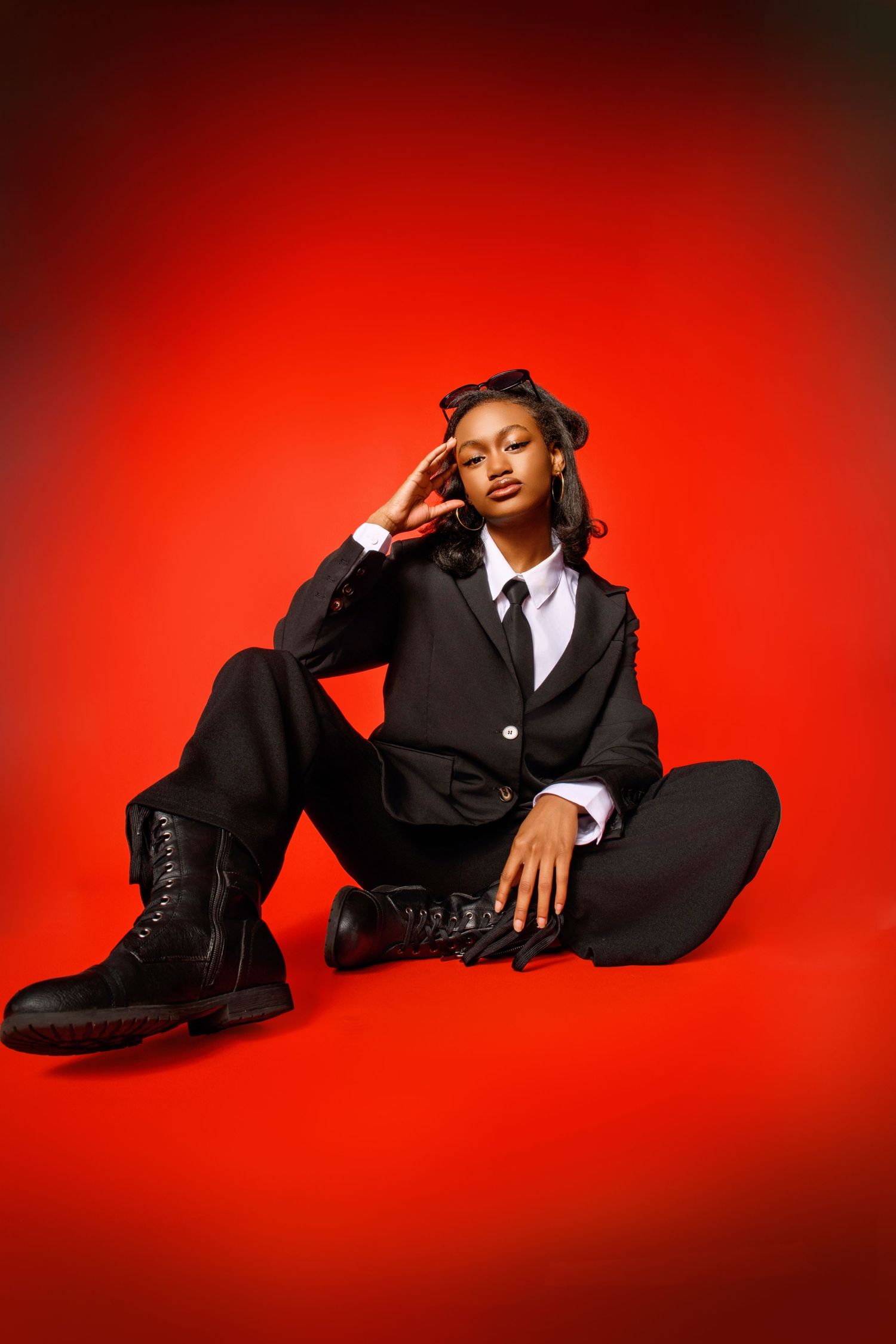 Fashion model in black suit poses dramatically on bright red studio floor.