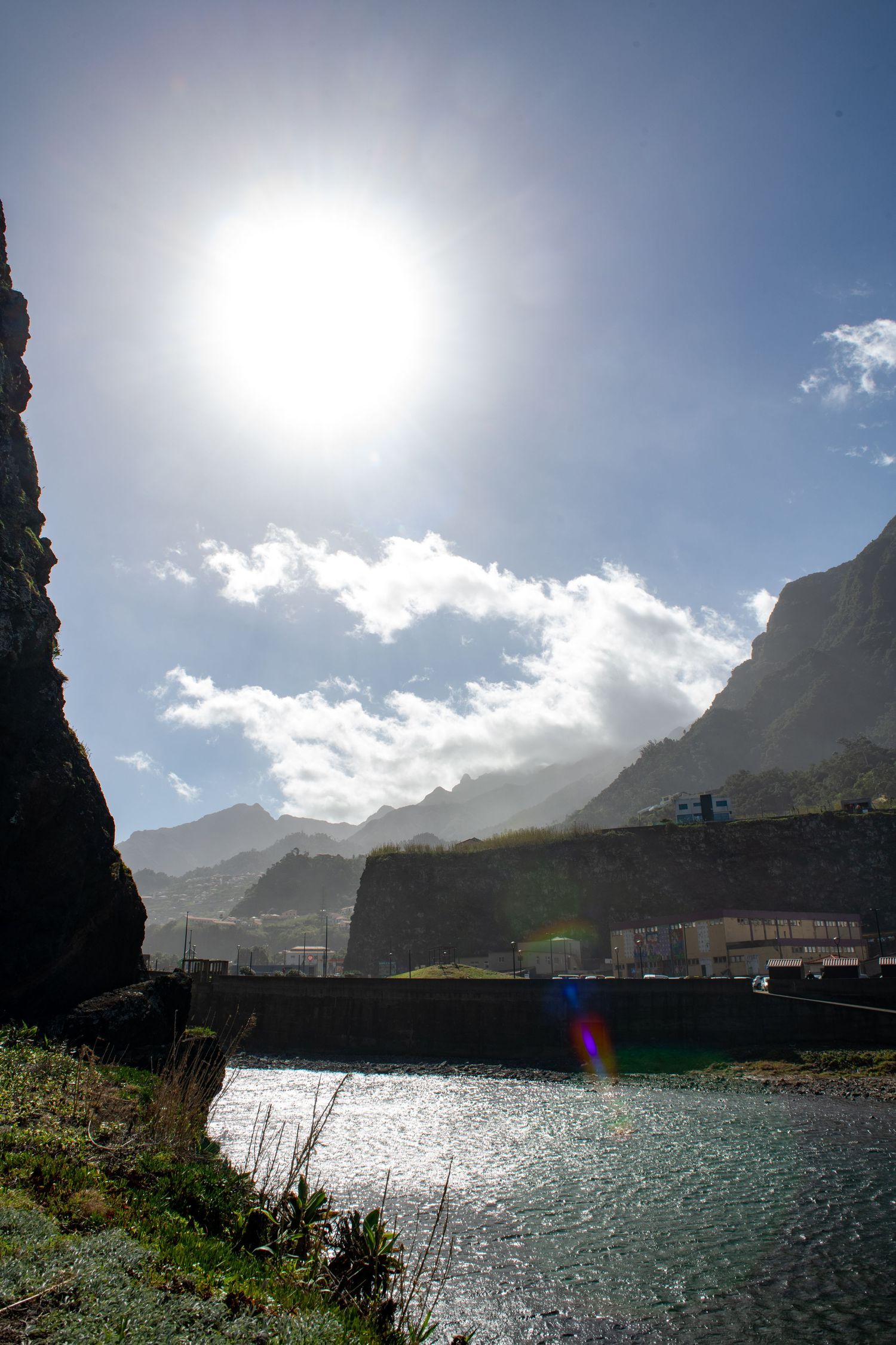 Sunlit harbor view with mountains silhouetted against bright sky and sparkling water.