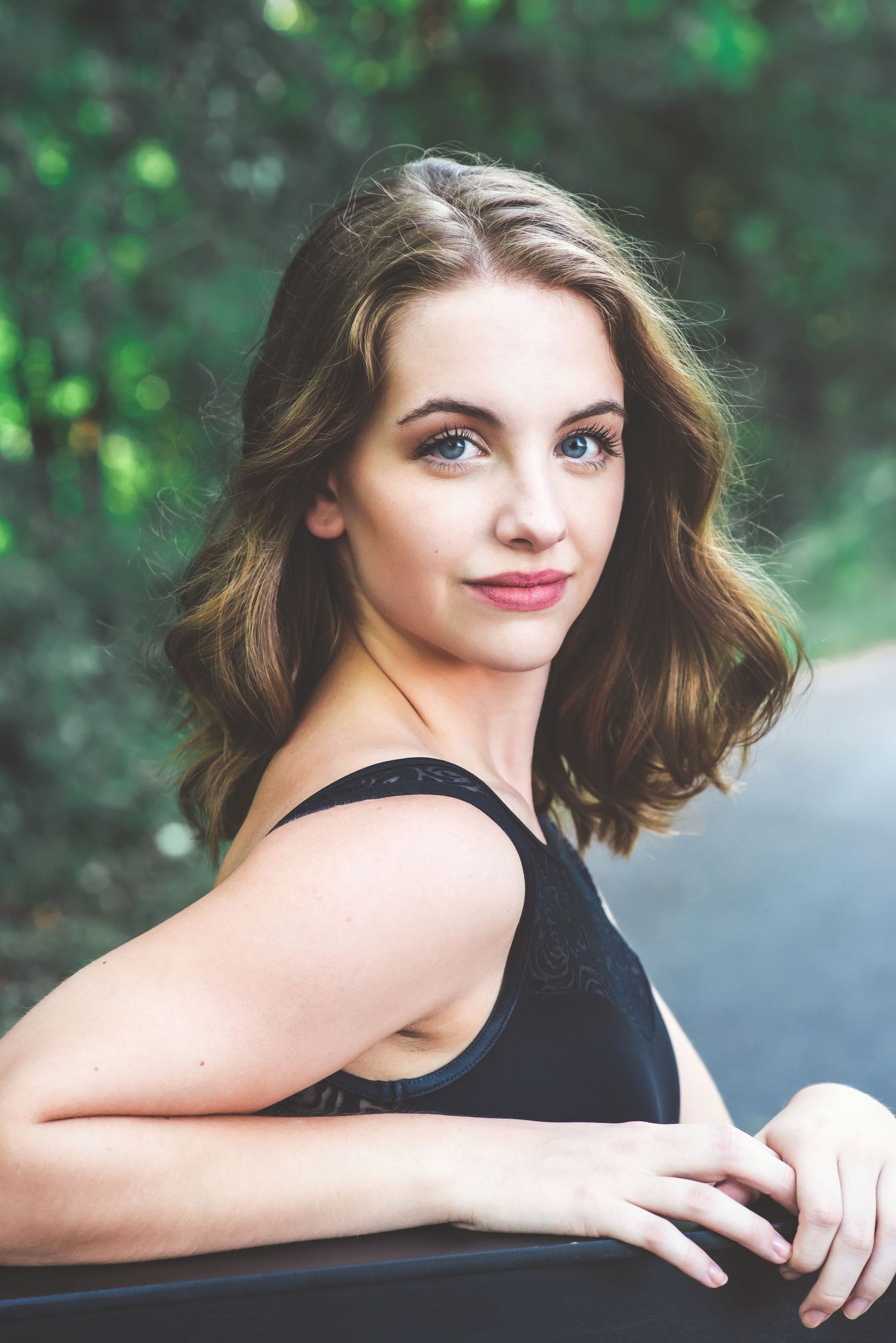 Portrait series in natural setting with black top and soft lighting against green foliage background.