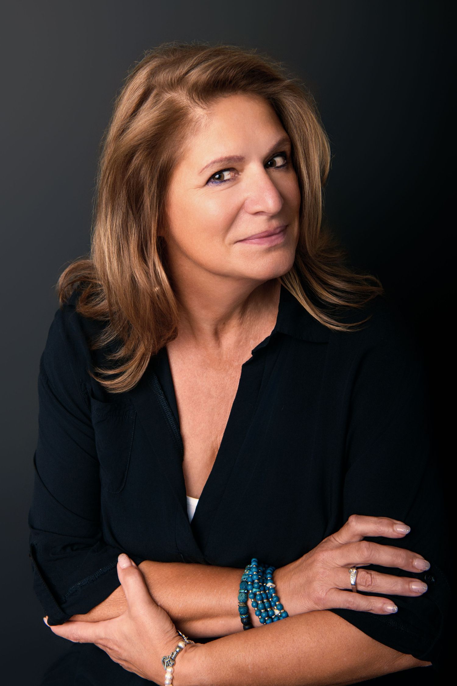 Studio portrait of woman in dark blazer with layered hair against black background.