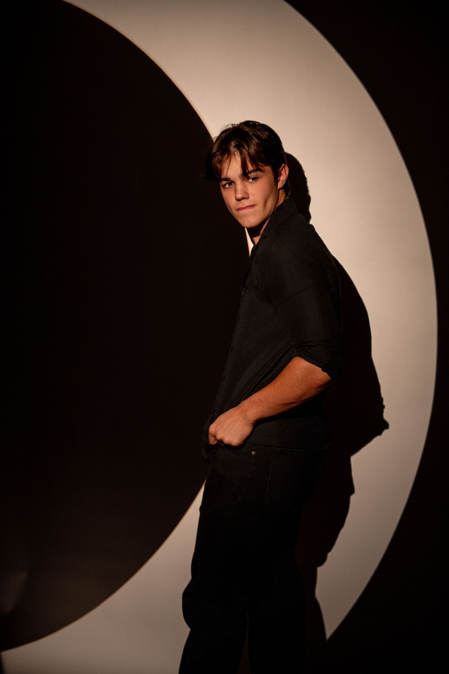 Dramatic portrait with person in dark clothing against curved light backdrop.