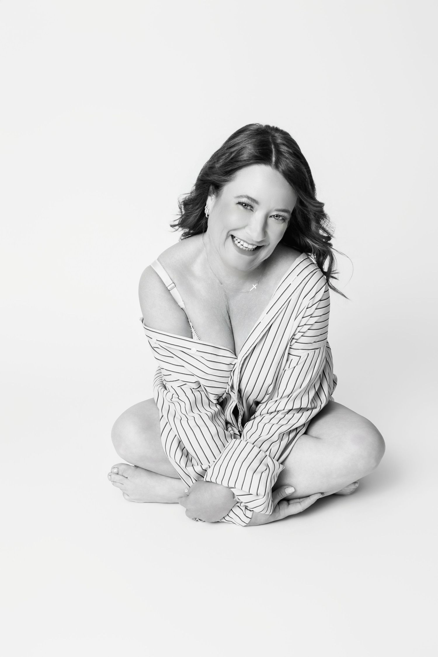 Joyful studio portrait in oversized striped shirt against minimalist white background.