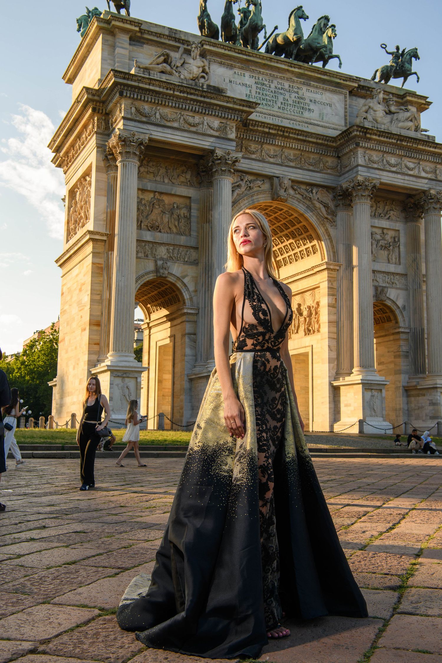 Elegant black dress photoshoot in front of historic triumphal arch at sunset.