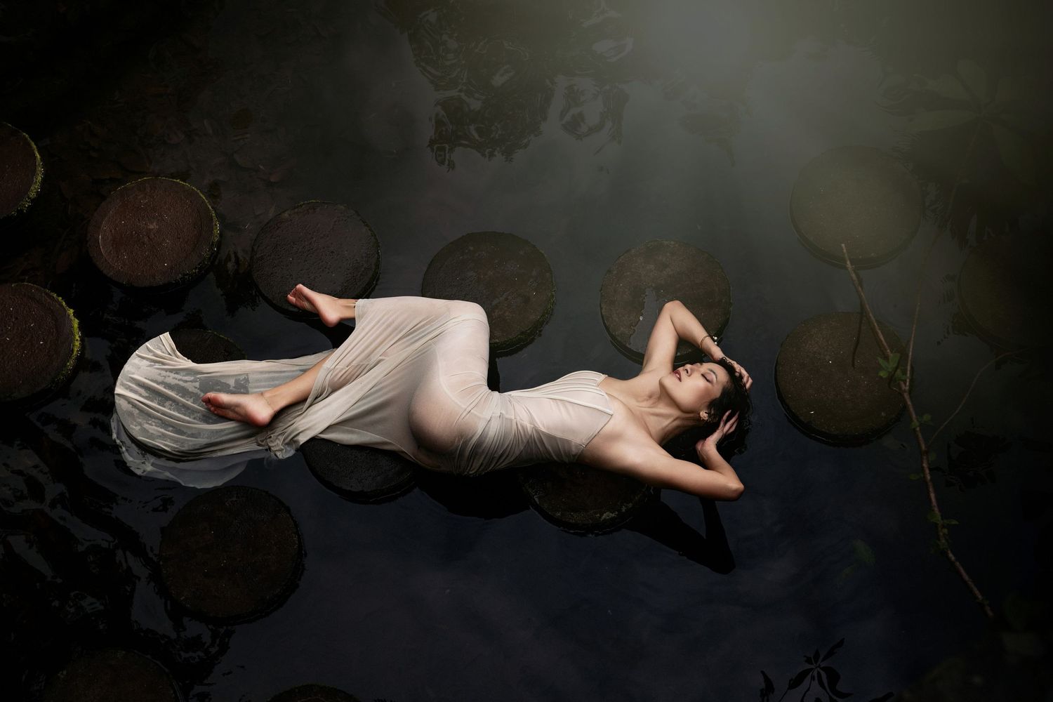 Artistic portrait of figure reclining on dark surface with flowing white fabric.