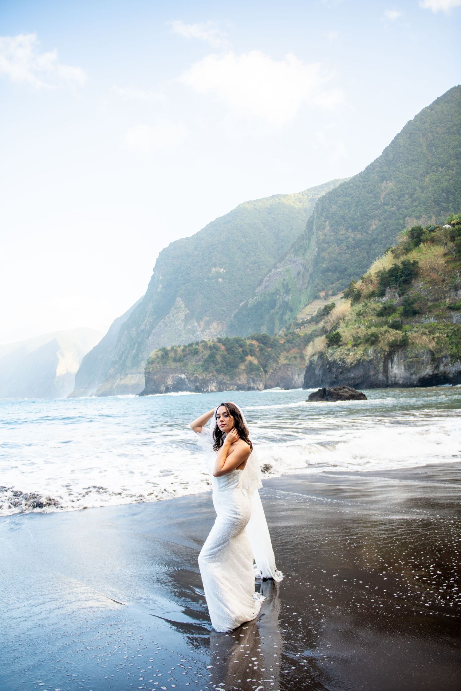 Ethereal beach photography session with flowing white dress against dramatic coastal cliffs.