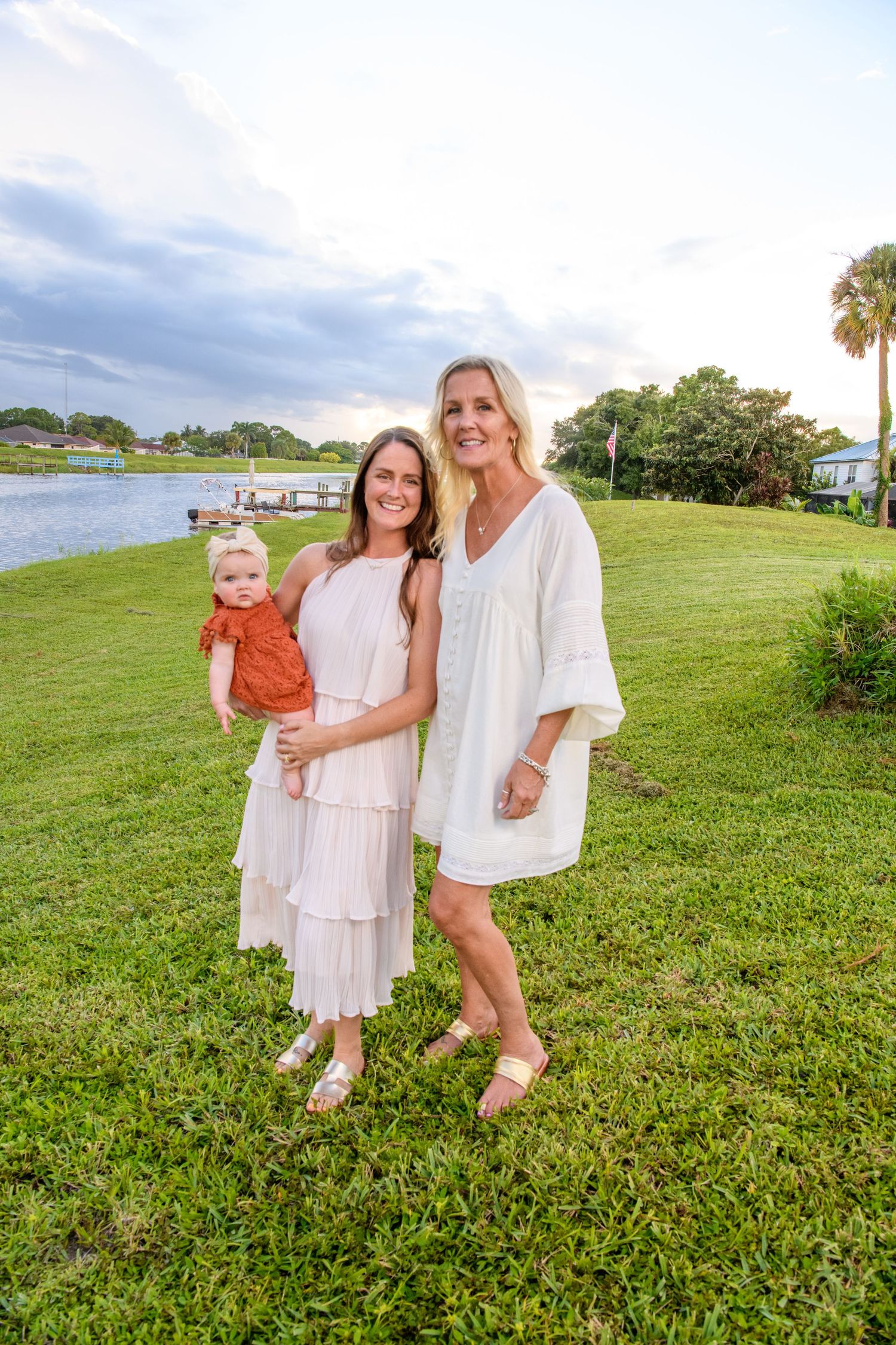 Group wearing white outfits poses together on grassy hillside during sunset.