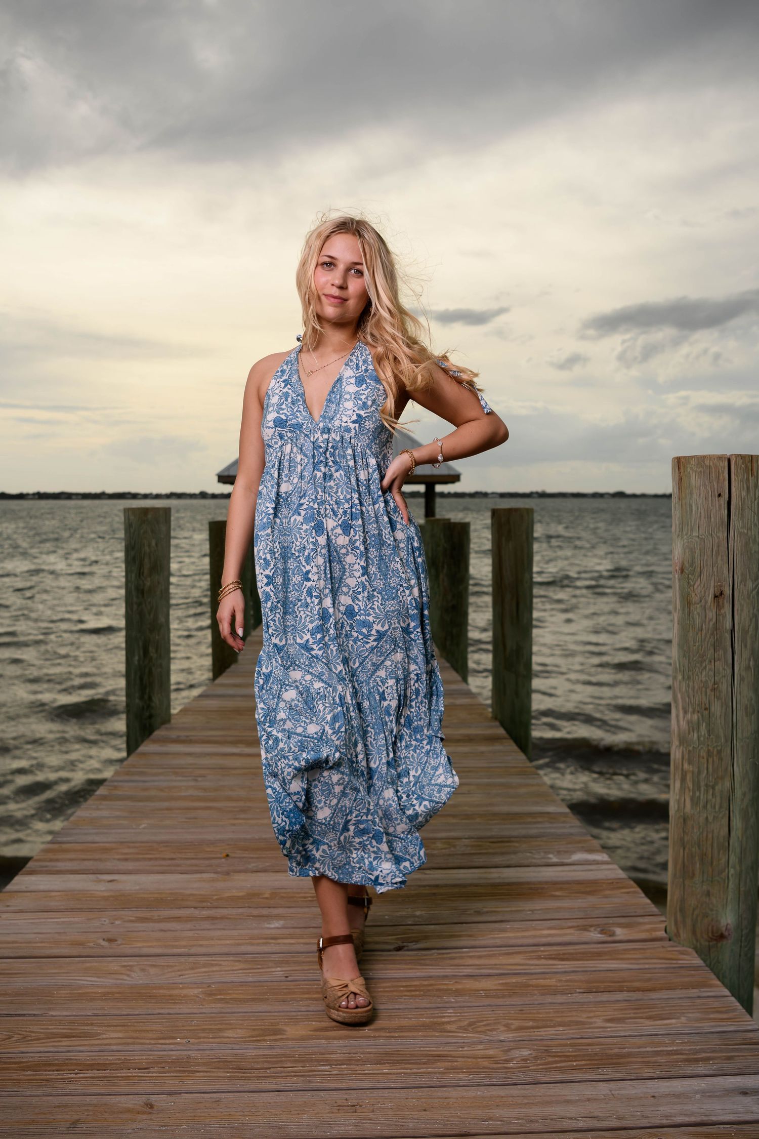 A series of photos on a wooden dock showing someone in a blue floral sundress posing by the water.